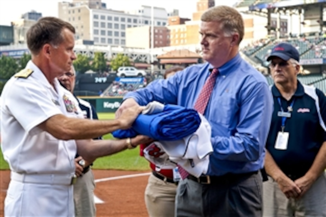 Navy Adm. James A. Winnefeld Jr., vice chairman of the Joint Chiefs of Staff, presents a small version of the USS Cleveland's battle flag to Jim Folk, vice president of ballpark operations for the Cleveland Indians, at Progressive Field in Cleveland, Aug. 27, 2012. World War II Navy veteran and baseball Hall of Fame pitcher Bob Feller gave the flag to the USS Cleveland six years ago. 