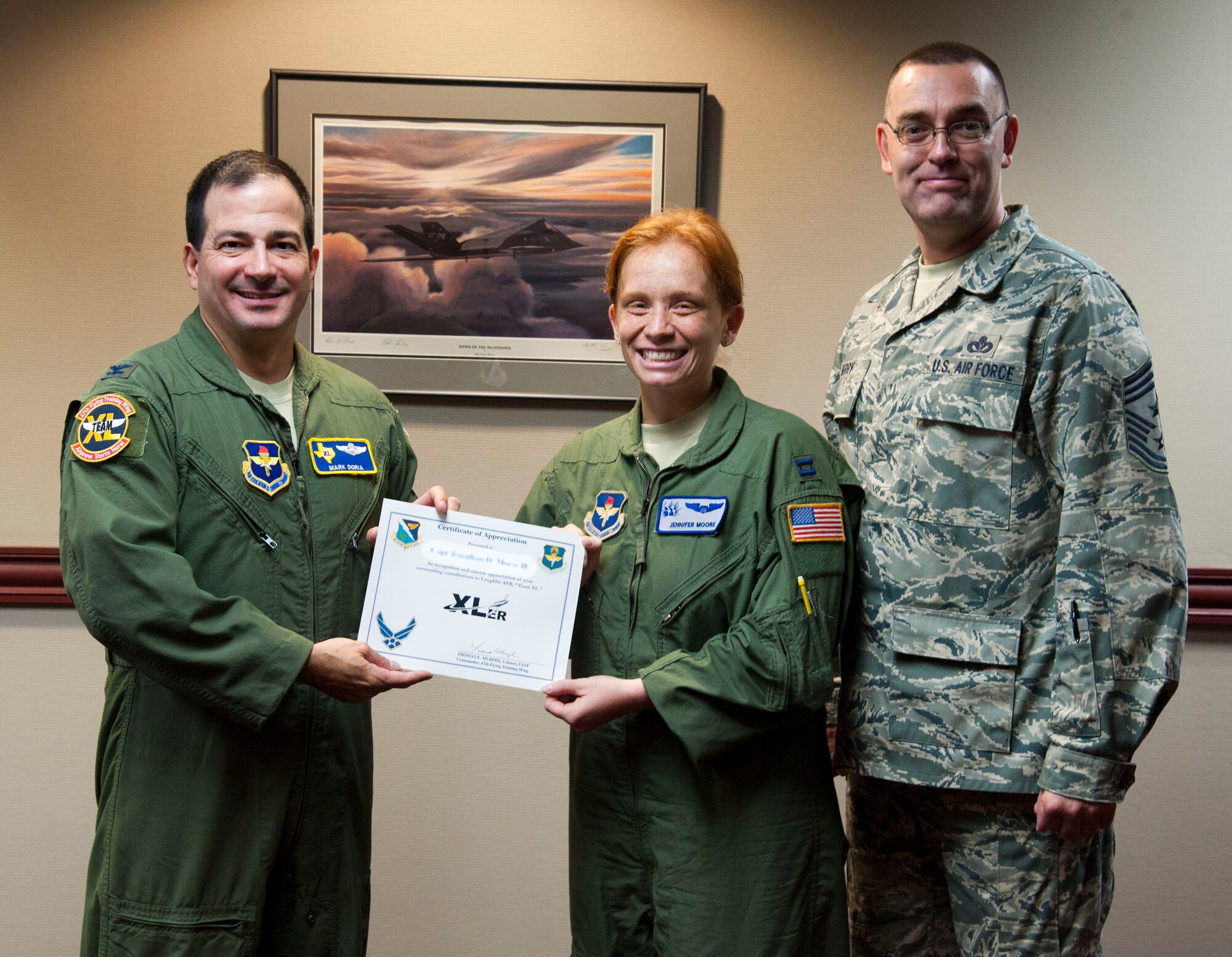 Capt. Jennifer Moore, 47th Student Squadron transition flight commander, poses with Col. Mark Doria, 47th Flying Training Wing vice commander, and Chief Master Sgt. Garry Berry, 47th FTW command chief, after being presented the XLer of the week award at Laughlin Air Force Base, Texas, Aug. 8, 2012. The XLer is a weekly award chosen by wing leadership and given to those who consistently make outstanding contributions to Laughlin and their unit. (U.S. Air Force photo illustration/Airman 1st Class Nathan Maysonet)