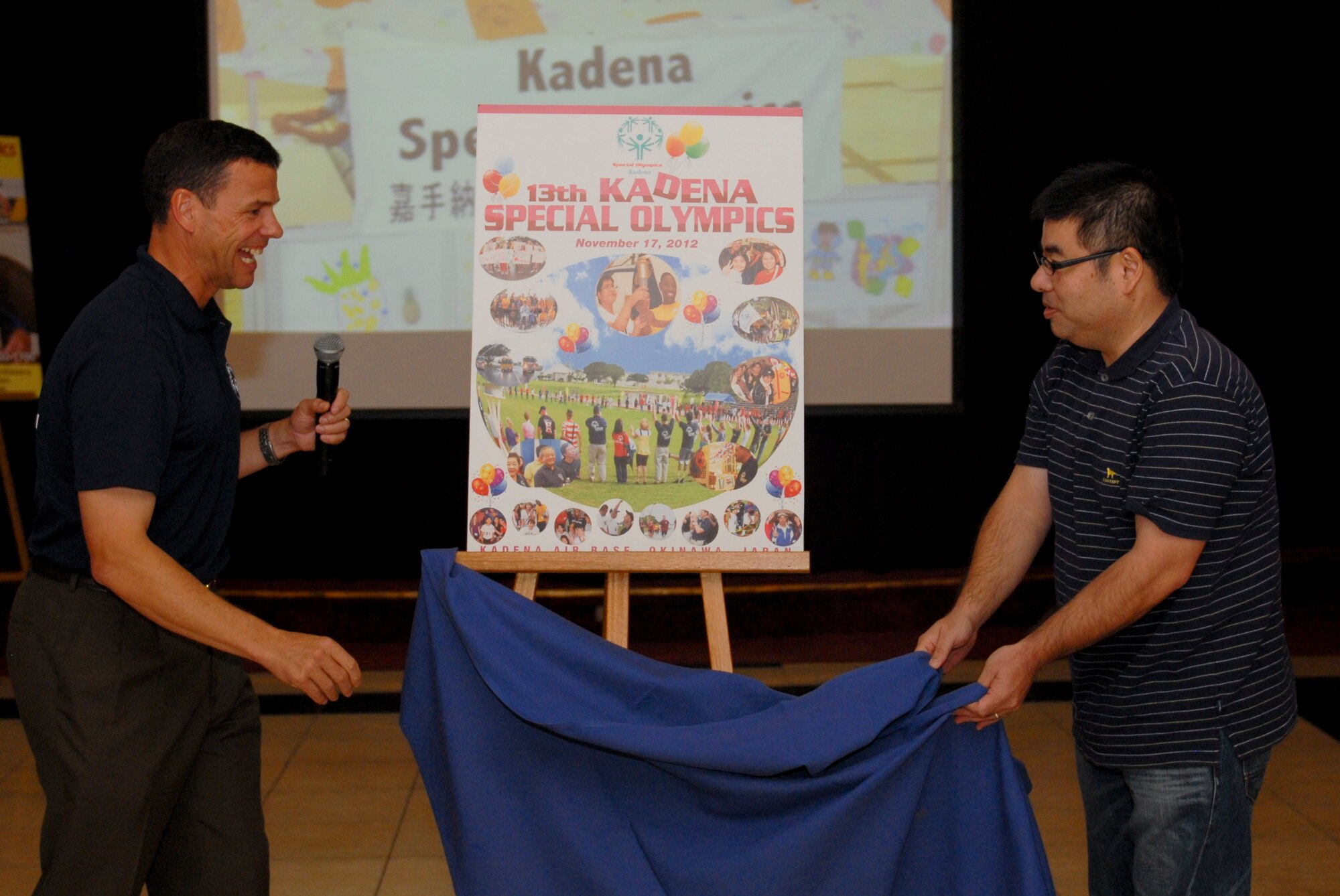 U.S. Air Force Brig. Gen. Matt Molloy, 18th Wing commander, and Takeshi Miyazato-Sama, Ikemiya Shokai Print Co. Kadena Special Olympics poster developer, unveil the 2012 KSO poster, designed by Miyazato-Sama, at the 2012 KSO Pep Rally on Kadena Air Base, Japan, Aug. 28, 2012. The poster is printed and displayed in prominent locations around the base with the purpose of attracting, promoting, and informing the community. So far members of the 18th Civil Engineer Squadron fire department raised more than $27,000 that will go toward this year’s KSO. (U.S. Air Force photo/Airman 1st Class Hailey R. Davis)