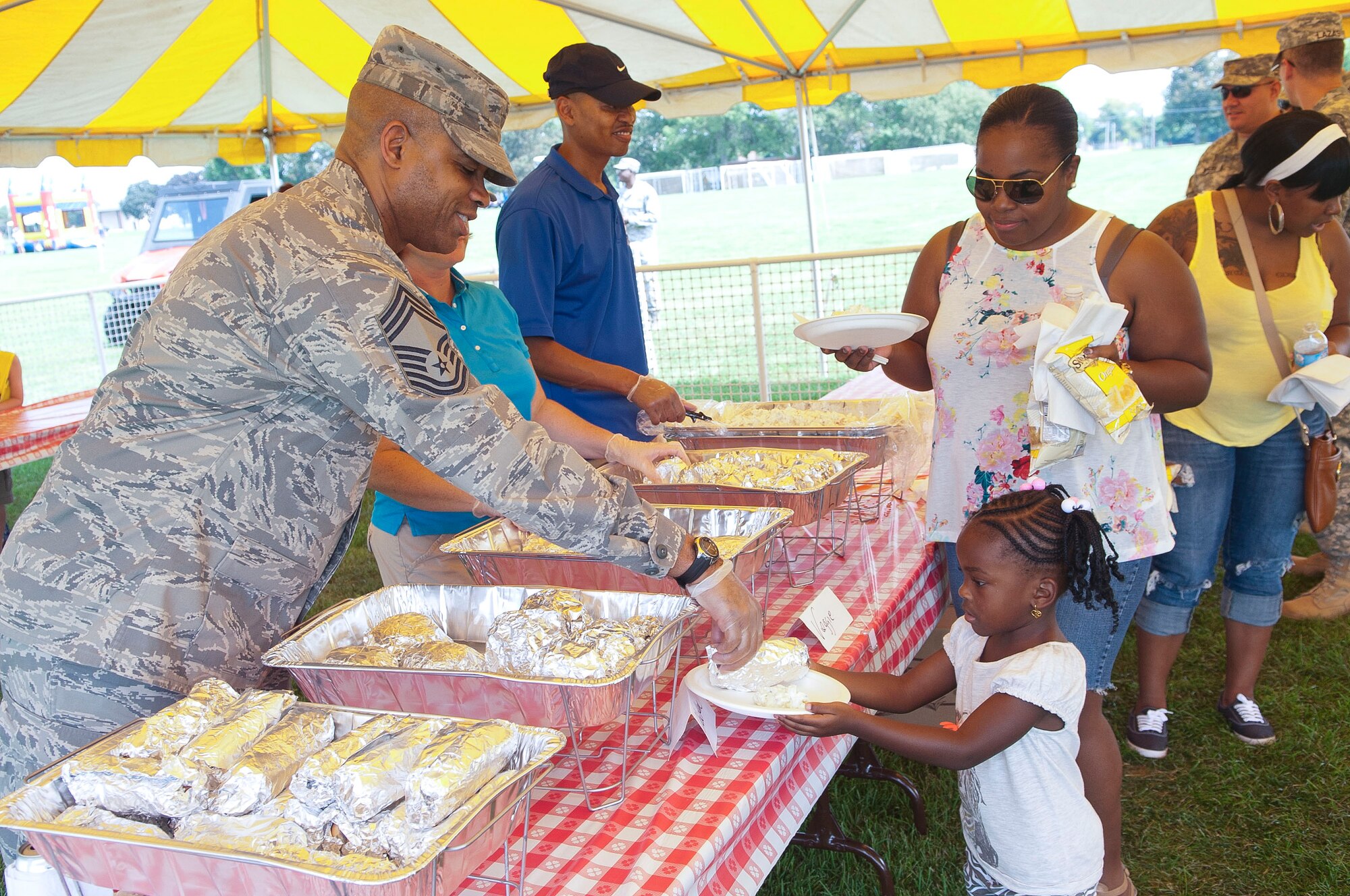 Chief Master Sgt. Vince Burrell, 87th Air Base Wing Command Post command and control functional manager, passes a hotdog to Brianna Sears, 4, daughter of Petty Officer 2nd Class Kevin Sears, VR-64 avionics maintenance technician, while her mother, Renetia, looks on Aug. 24 at the Joint Base McGuire-Dix-Lakehurst Annual Summer Picnic held on Doughboy Field. (U.S. Air Force photo by Wayne Russell/Released)