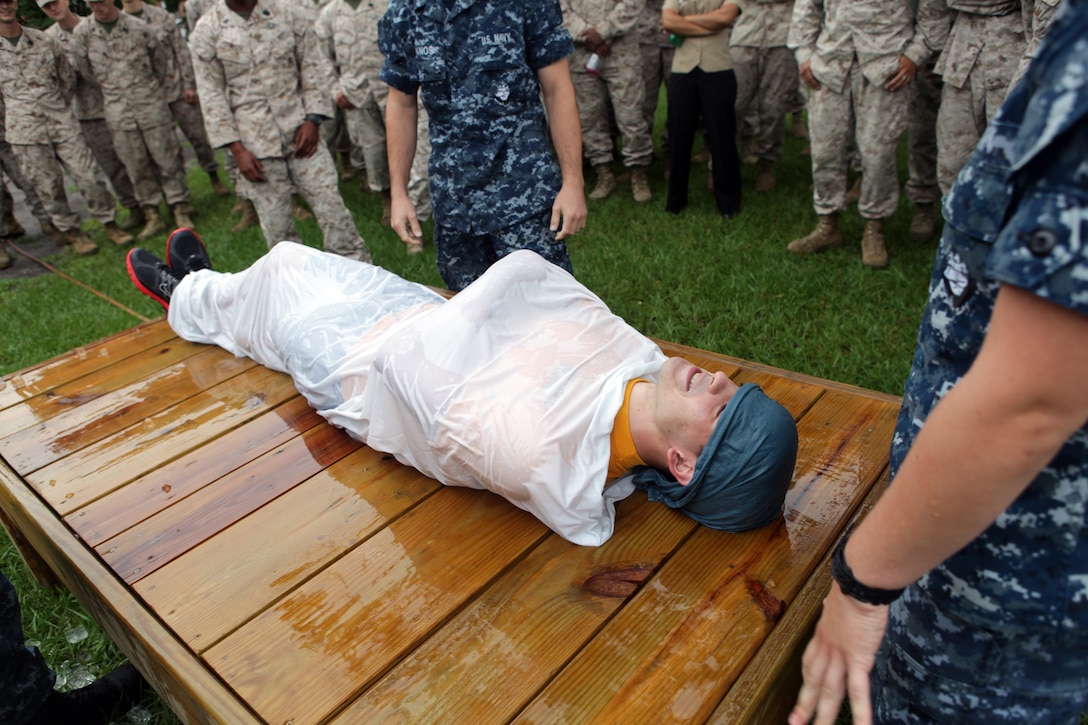 Navy Petty Officer 3rd Class Ryan Adams is being used as an example victim for cooling a heat casualty at the bi-annual hot weather standard operating procedure training aboard Marine Corps Base Camp Lejeune Aug. 24. Adams is demonstrating the ‘burrito’ method used to cool a heat related injury victim.