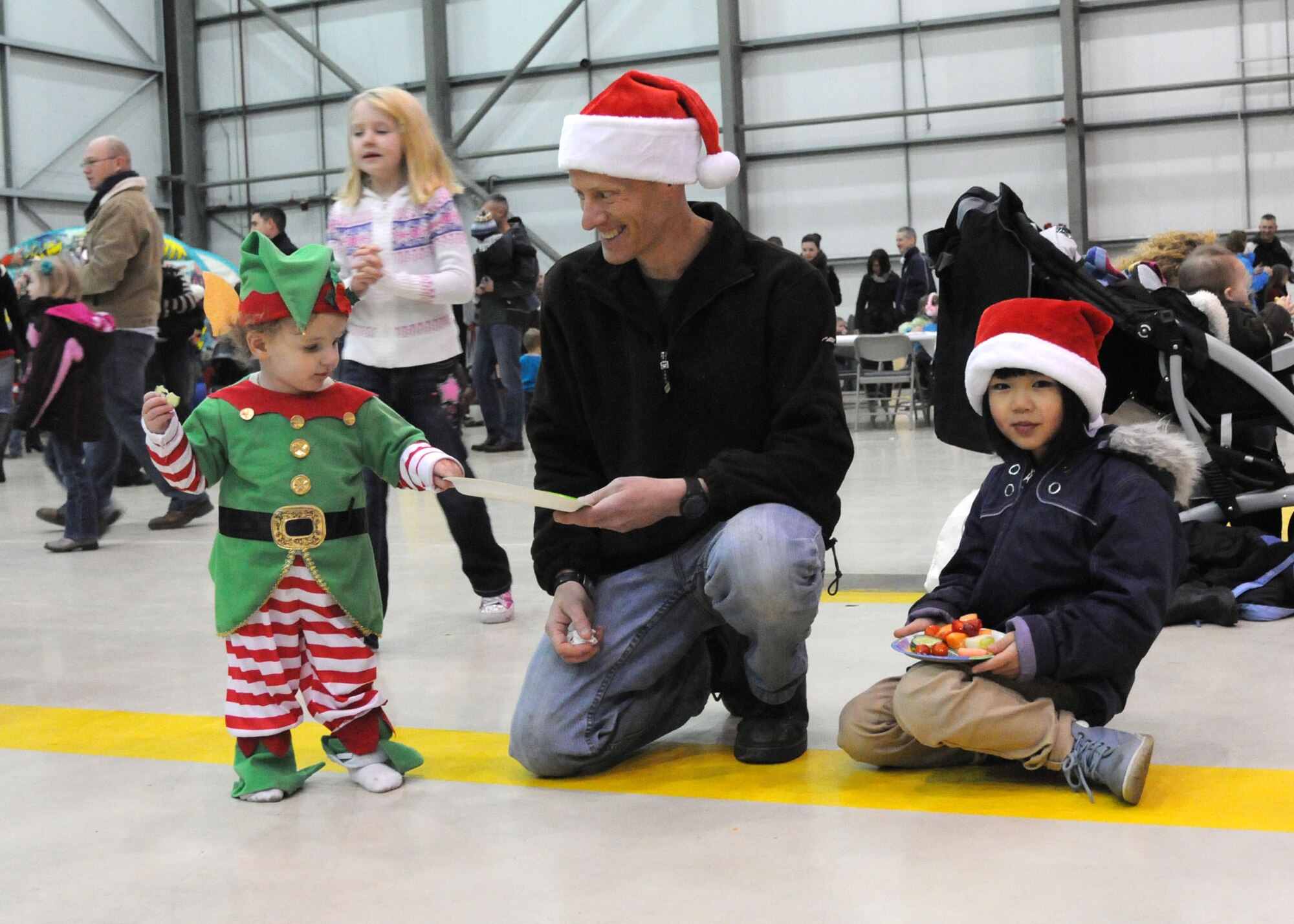 Lt Col. Chris Bennett, 100th Operations Support Squadron commander from Houston, Alaska, shares a snack with his children, Ashton 17 mo., and Emma 8, at the 100th Maintenance Group Children's Christmas Party Dec. 1, 2012, at Hangar 803 at RAF Mildenhall, England. The party had many activities to include a meet and greet with Santa, cookie decorating, bingo, bouncy castles, face painting and coloring. (U.S. Air Force photo by Airman 1st Class Kelsey A.L. Waters/Released)