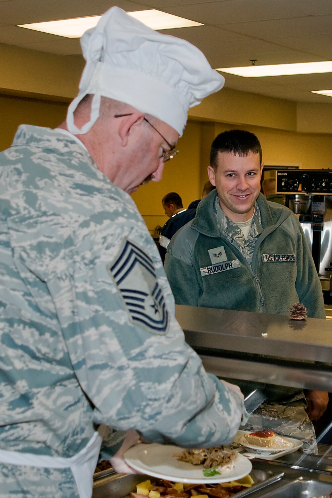 GRISSOM AIR RESERVE BASE, Ind. -- Senior Airman Steven Rudolph, 434th Maintenance Squadron crew chief, gives a grin as Chief Master Sgt. Glen Johnson, 434th Civil Engineer Squadron infrastructure superintendant, dishes out a special holiday meal. Senior leadership from the 434th Air Refueling Wing rolled up their sleeves to serve a holiday meal and greet Airmen during a recent Unit Training Assembly. (U.S. Air Force photo/Senior Airman Jami K. Lancette)