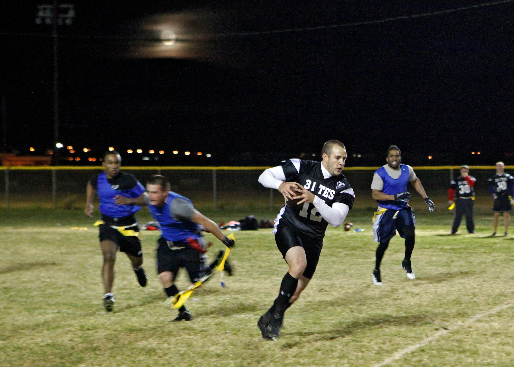 Justin Dion, 31st Test and Evaluation Squadron quarterback, rushes against a group of 412th Medical Group defenders during the Edwards intramural flag football championship at Wings Field Nov. 29. The 31st TES Desert Pirates defeated the 412th MDG Desert Medics 32-21. (U.S. Air Force photo by Jet Fabara)