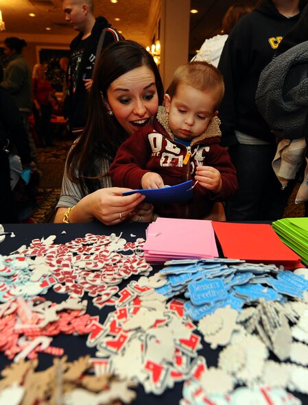 Two-year-old Jackson Buehler and his mom, dependents of Capt. Trent Buehler, 55th Dental Squadron, look through piles of holiday ornaments they can select to build their own tree ornament while attending the Christmas Tree Lighting reception at the Patriot Club on Offutt Air Force Base, Neb., Nov. 29. The tree lighting and festivities that follow draws hundreds of families each year. (U.S. Air Force photo by Josh Plueger/Released)