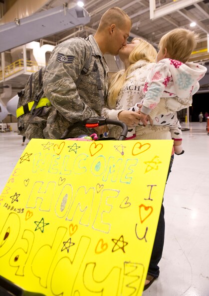 Air National Guard Staff Sgt. Jason Mann, 116th Maintenance Squadron, shares a kiss with his wife Cassandra while his daughter Emma looks on upon his return from a deployment in the early morning hours of Dec. 3 at Robins Air Force Base, Ga.  Approximately 50 Team JSTARS operations, maintenance and support personnel were returning home from a three month deployment to an undisclosed location in the Middle East. (National Guard photo by Master Sgt. Roger Parsons/Released)