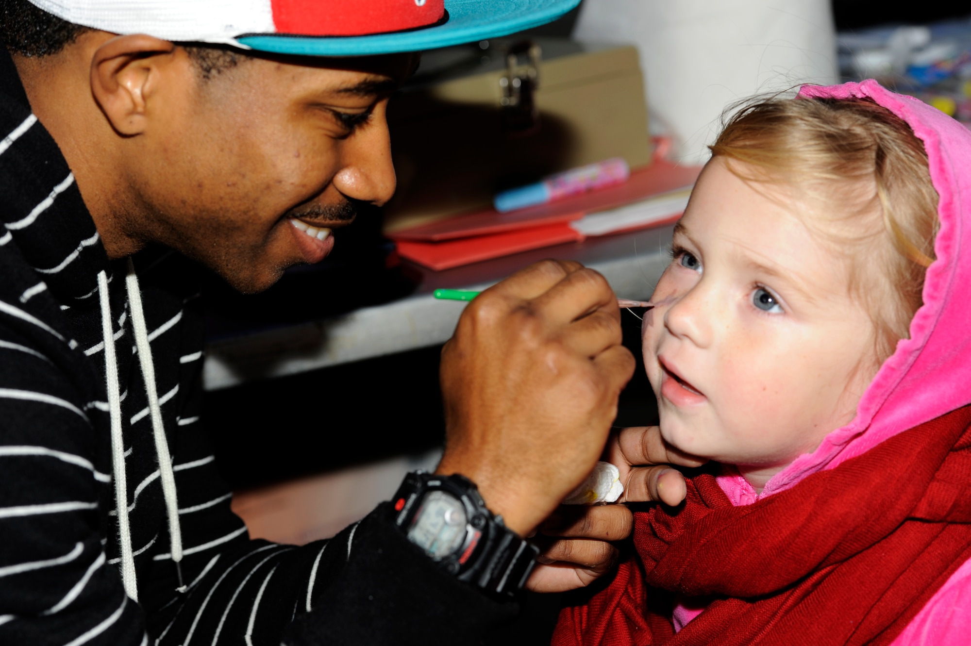 U.S. Air Force Airman 1st Class Terrence Crenshaw Jr., 18th Logistic Readiness Squadron vehicle maintainer and face-painting volunteer for the Tinsel Town holiday festival, paints a picture on Lily Grace Palmer's face during the event on Kadena Air Base, Japan, Dec. 1, 2012. Despite dark skies and a constant Okinawan drizzle in the air, the event gave a merry light to the crowd with games, children's rides, concessions, prize giveaways and concerts by several bands including country music star Trace Adkins during his USO tour. (U.S. Air Force photo/Senior Airman Maeson L. Elleman)