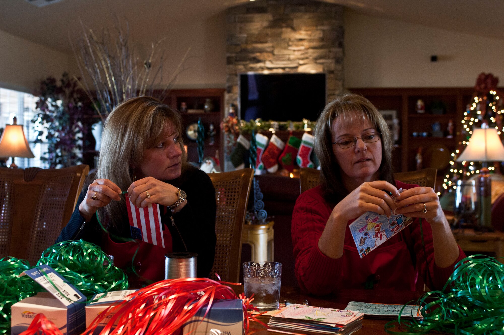 Terrie Hecker, wife of U.S. Air Force Col. James Hecker, 432d Wing commander, and Shannon Grynkewich, wife of Col. Alex Grynkewich, 57th Wing vice commander, tie ribbons to Christmas cards made by children from local schools during the 2012 Holiday Cookie Drive Dec. 03, 2012, at Nellis Air Force Base, Nev. The Holiday Cookie Drive is a tradition where donated confectionary delicacies are gifted to single Airmen living in the dormitories on Nellis and Creech Air Force Bases in an effort to bring the presence of family to Airmen during the holidays. (U.S. Air Force by Senior Airman Daniel Hughes)
