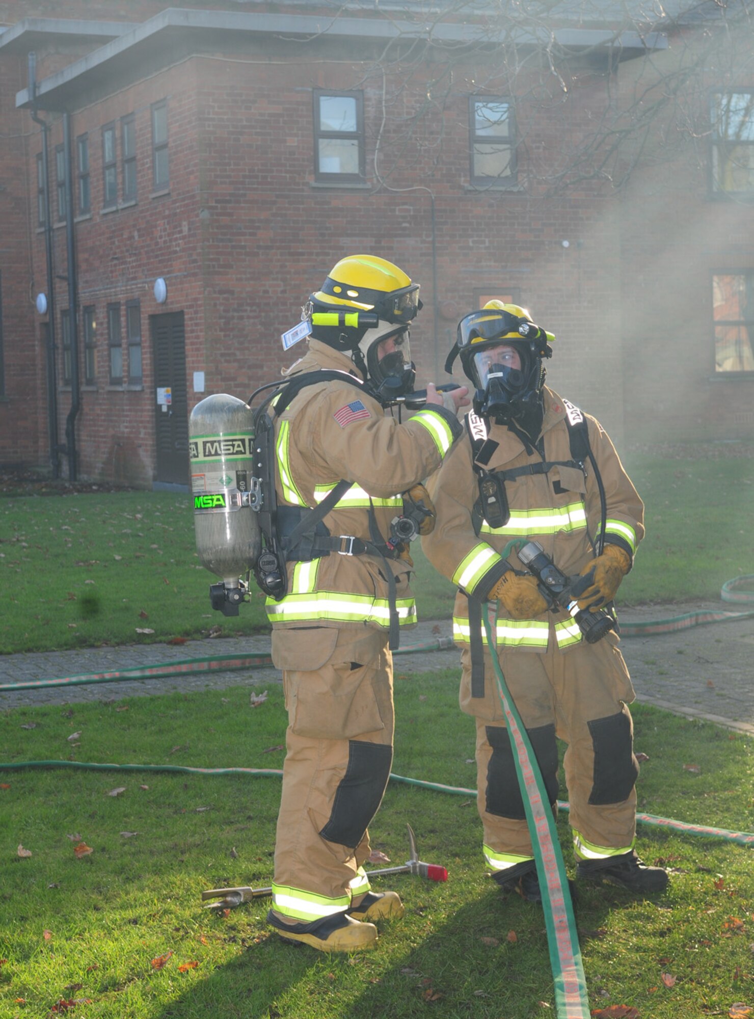 Firefighters Malcolm Strickland, left, and Airman 1st Class Stuart Hassel, 100th Civil Engineer Squadron Fire Department, discuss the setup of the casualty collection point outside building 438 as they wait to be called to respond inside the building Dec. 3, 2012, at RAF Mildenhall, England. During an operational readiness exercise scenario, the 100th Security Forces Squadron building was filled with smoke, and firefighters responded and rescued three simulated casualties. The ORE, which runs to Dec. 7, is one of many in preparation for a combined unit inspection in 2013. (U.S. Air Force photo by Karen Abeyasekere/Released)
