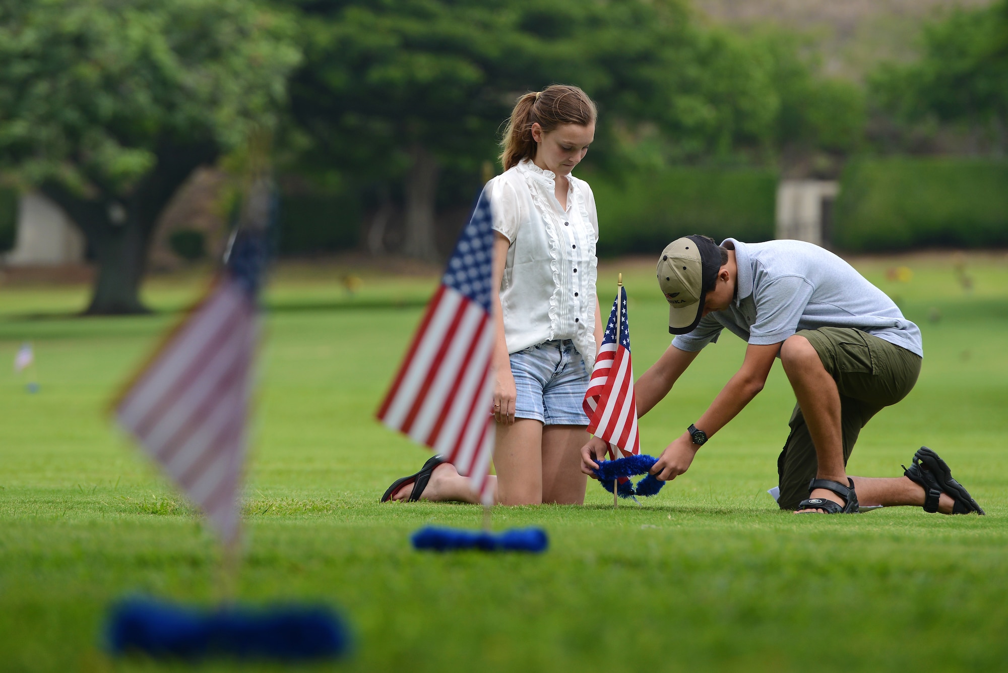 Emma McLeod and Chris Friedrichs places an American flag and handmade lei at the top of a headstone, Dec. 2, 2012, at the National Cemetery of the Pacific, at Punchbowl in Honolulu. McLeod, Friedrichs and eight other volunteers placed 92 flags among the 34,000 gravesites on the grounds of the cemetery to honor the men who lost their lives at Hickam Field on Dec. 7, 1941. The teenagers, with the help of Jessie Higa, started the project to place American flags and leis at the gravesites of the fallen Hickam Field Airmen for a community service project in 2011. They had a lei making party and watched the World War II series, Band of Brothers, while making the leis. (U.S. Air Force photo/Staff Sgt. Mike Meares)