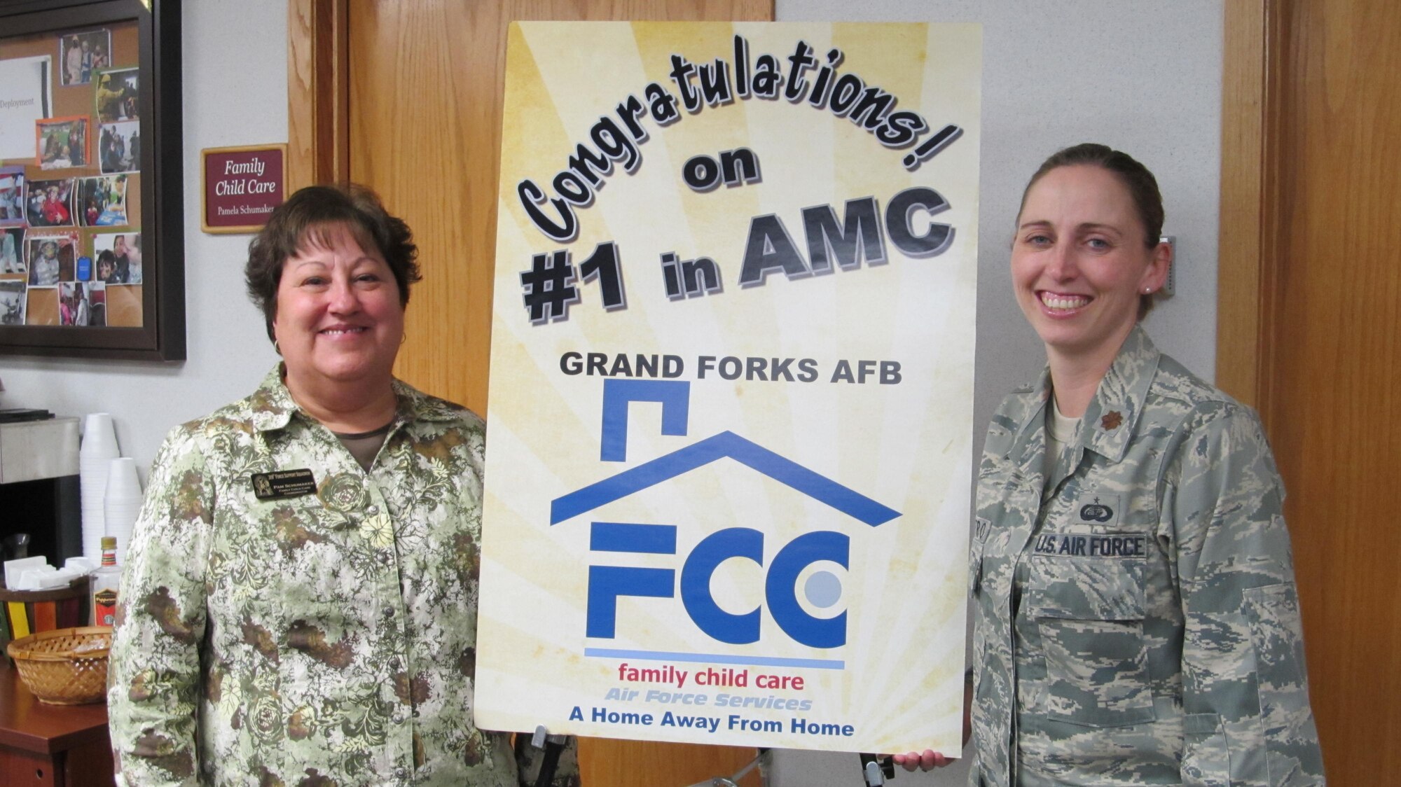 Pamela Schumaker, Airman & Family Readiness Center family child care coordinator, and Maj. Regina Castro, 319th Force Support Squadron commander, stand with a poster recognizing the Grand Forks Air Force Base Family Child Care as the best in the Air Mobility Command, Nov. 8 here at the A&FRC. The A&FRC worked with more than 30 agencies, to achieve this special recognition. (Courtesy photo)