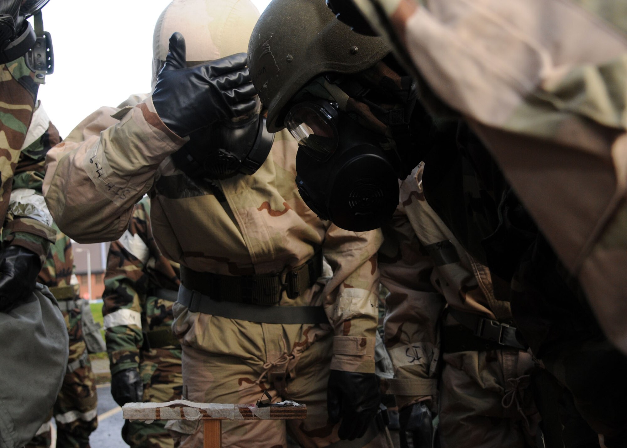 Airmen gather around mock M-9 tape to check it for contamination during an exercise at the Ability to Survive and Operate Rodeo Dec. 5, 2012, in the Hardstand Fitness Center, at RAF Mildenhall, England. The Airmen also had to perform self-aid buddy care and demonstrate their understanding of mission-orientated protective posture levels. (U.S. Air Force photo by Airman 1st Class Kelsey Waters/Released)