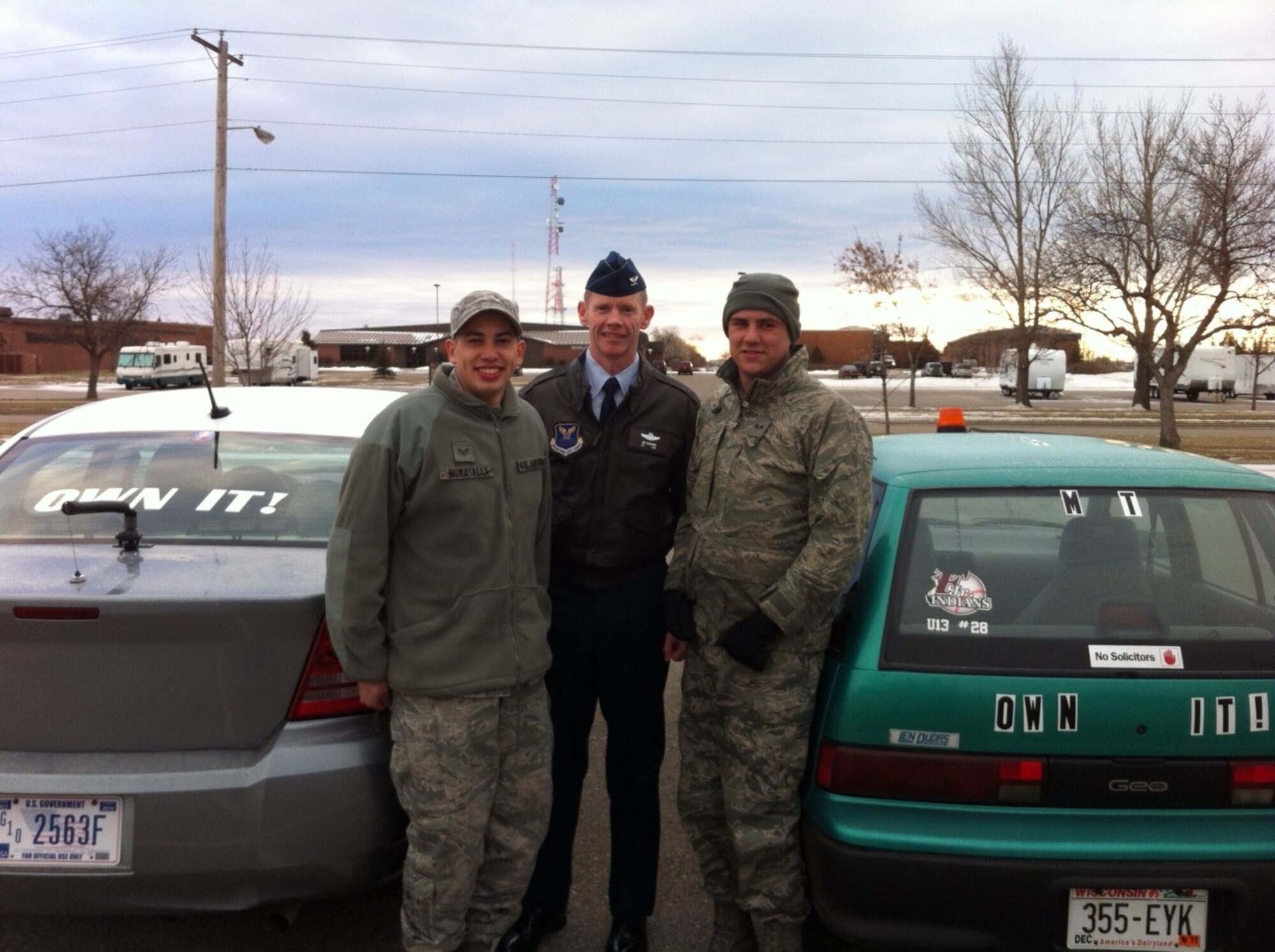MINOT AIR FORCE BASE, N.D. -- Senior Airman Bernardo Muratalla (left), 69th Aircraft Maintenance Unit crew chief, and Senior Airman Neil Ayers (right), 23rd AMU crew chief, pose for a photo with Col. James Dawkins, 5th Bomb Wing commander, in front of Murtalla's "OWN IT" car. The two Airmen wanted to find ways to boost morale and pride in Minot's mission and decided to create their own version of a morale car. Ayers has also found other ways to showcase his pride and boost morale by spelling out "OWN IT" in Christmas lights on his home in base housing, letting everyone in the neighborhood see how he feels about Minot's mission. (Courtesy photo)