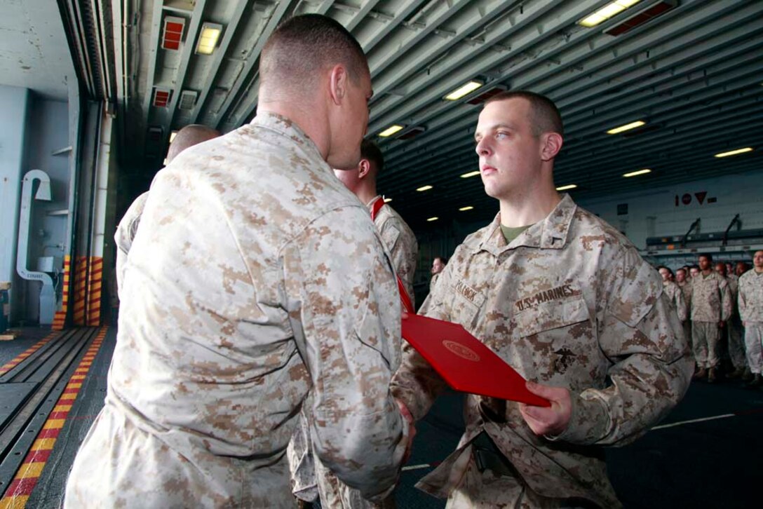 Newly promoted Private First Class John M. Pollock, CH-46E airframes mechanic, Marine Medium Helicopter Squadron 364 (Rein.), 15th Marine Expeditionary Unit, receives his promotion warrant from his commanding officer, Lt. Col. Ned M. Biehl, after being promoted during a squadron promotion and awards ceremony in the hangar bay of the USS Peleliu, Dec. 1. Marine Medium Helicopter Squadron 364 (Rein.) serves as the aviation combat element for the 15th MEU. The 15th MEU is deployed as part of the Peleliu Amphibious Ready Group as a U.S. Central Command theater reserve force, providing support for maritime security operations and theater security cooperation efforts in the U.S. 5th Fleet area of responsibility. Pollock, 20, is from San Antonio. (U.S. Marine Corps photo by Cpl. John Robbart III/Released)