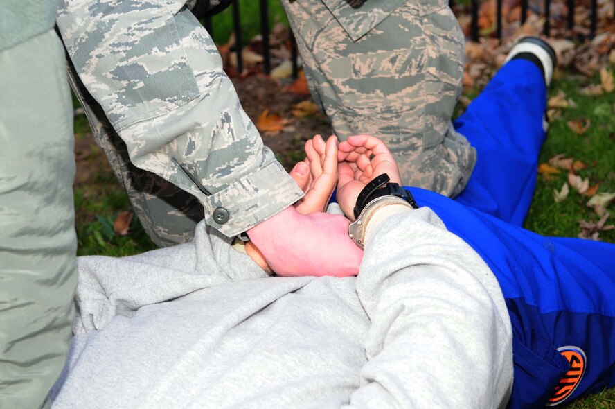 A member of the 100th Security Forces Squadron handcuffs a suspicious individual after he and two others entered RAF Mildenhall illegally by driving the wrong way through Gate 17 Dec. 4, 2012, as part of an operational readiness exercise scenario. Members from the 100th SFS quickly apprehended all three individuals, stopped traffic and set up a cordon after the scenario turned into a bomb threat because the driver left a suspicious package outside building 591. The ORE is one of many exercises in preparation for a combined unit inspection in 2013. (U.S. Air Force photo by Karen Abeyasekere/Released)