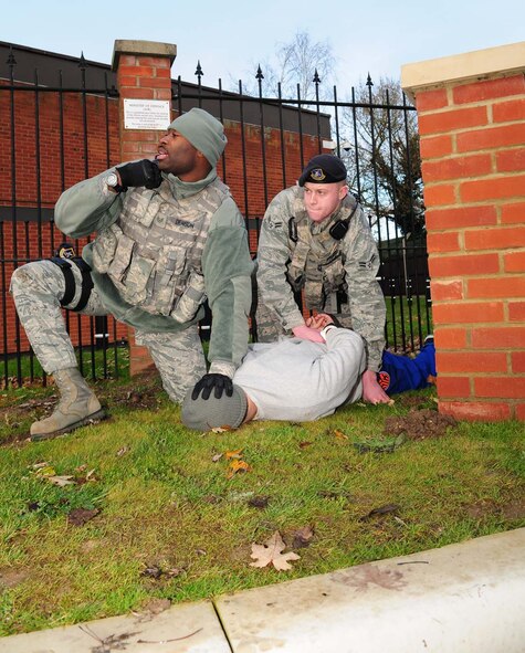 Staff Sgt. Michael Denson, left, 100th Security Forces Squadron combined controller, talks on his radio to the 100th SFS Base Defense Operations Center, informing them of a situation Dec. 4, 2012, during an operational readiness exercise at RAF Mildenhall, England. Denson, from Newark, N.J., and Airman 1st Class Bradley Pruzzo, 100th SFS response force member, from Detroit, Mich., held the suspect (played by Senior Airman Luis Ramos, 100th SFS response force leader, from Bronx, N.Y.) and searched him after he drove a car through Gate 17 the wrong way, pushing past the gate guards and illegally entering the base. The ORE is one of many exercises in preparation for a combined unit inspection in 2013. (U.S. Air Force photo by Karen Abeyasekere/Released)