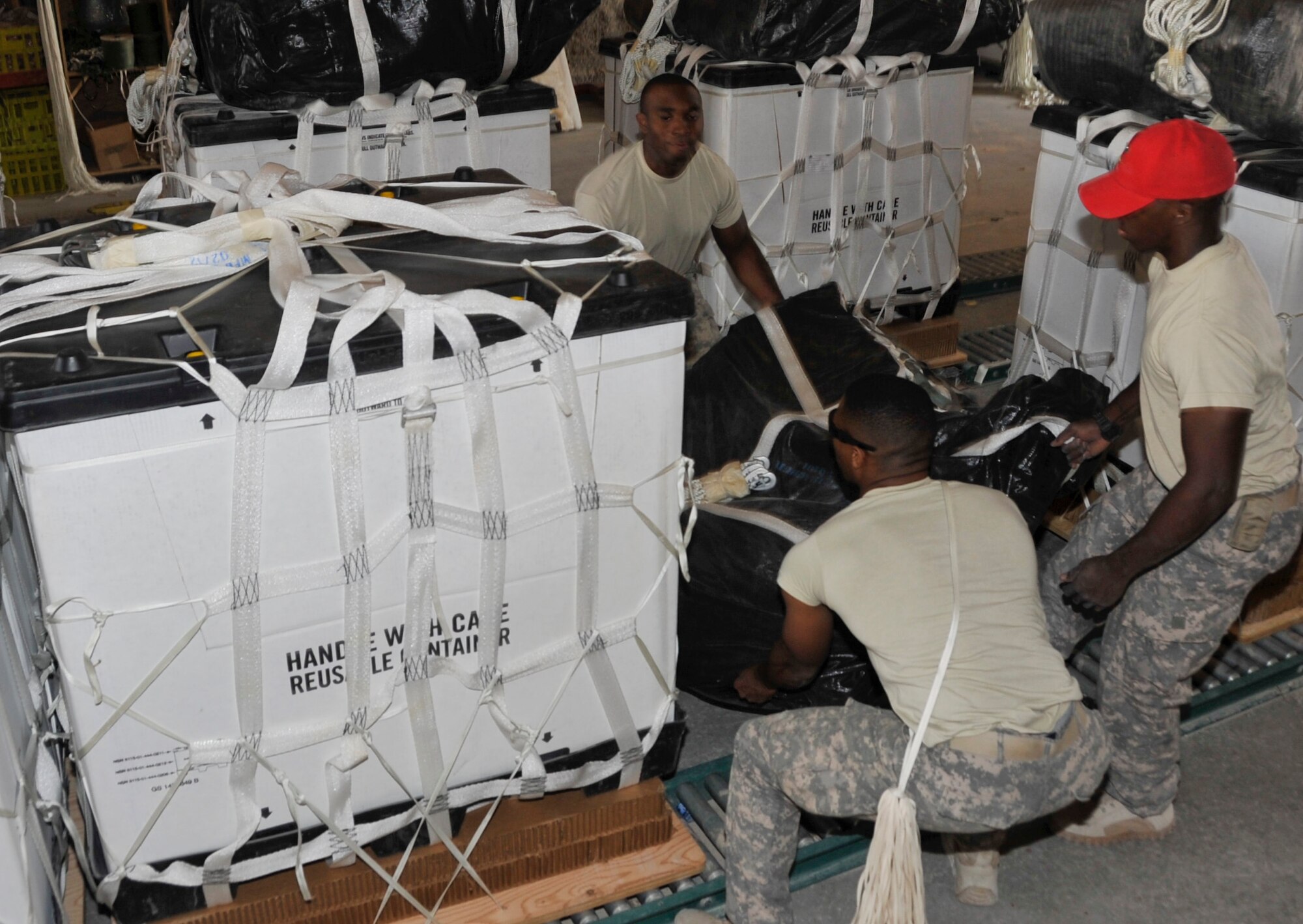 SOUTHWEST ASIA - (Left to right)Army Spc. Vacito Gumbs, Spc. Chimdi Ogbeka and Spc. Frank Bebbs, 421st Quartermaster Company Detachment 4 airdrop specialists, lift the 200-pound parachute to place on top of a bundle Dec. 4. The 24-man team rigs, drops and constructs approximately 670 bundles a month, which primarily containing food, water, fuel, building materials and wood. Gumbs, a native of the U.S. Virgin Islands, Ogbeka, a native of Powder Springs, Ga., and Bebbs, a native of Fayetteville, N.C., are deployed from Fort Valley, Ga. (U.S. Air Force photo/Senior Airman Bryan Swink)