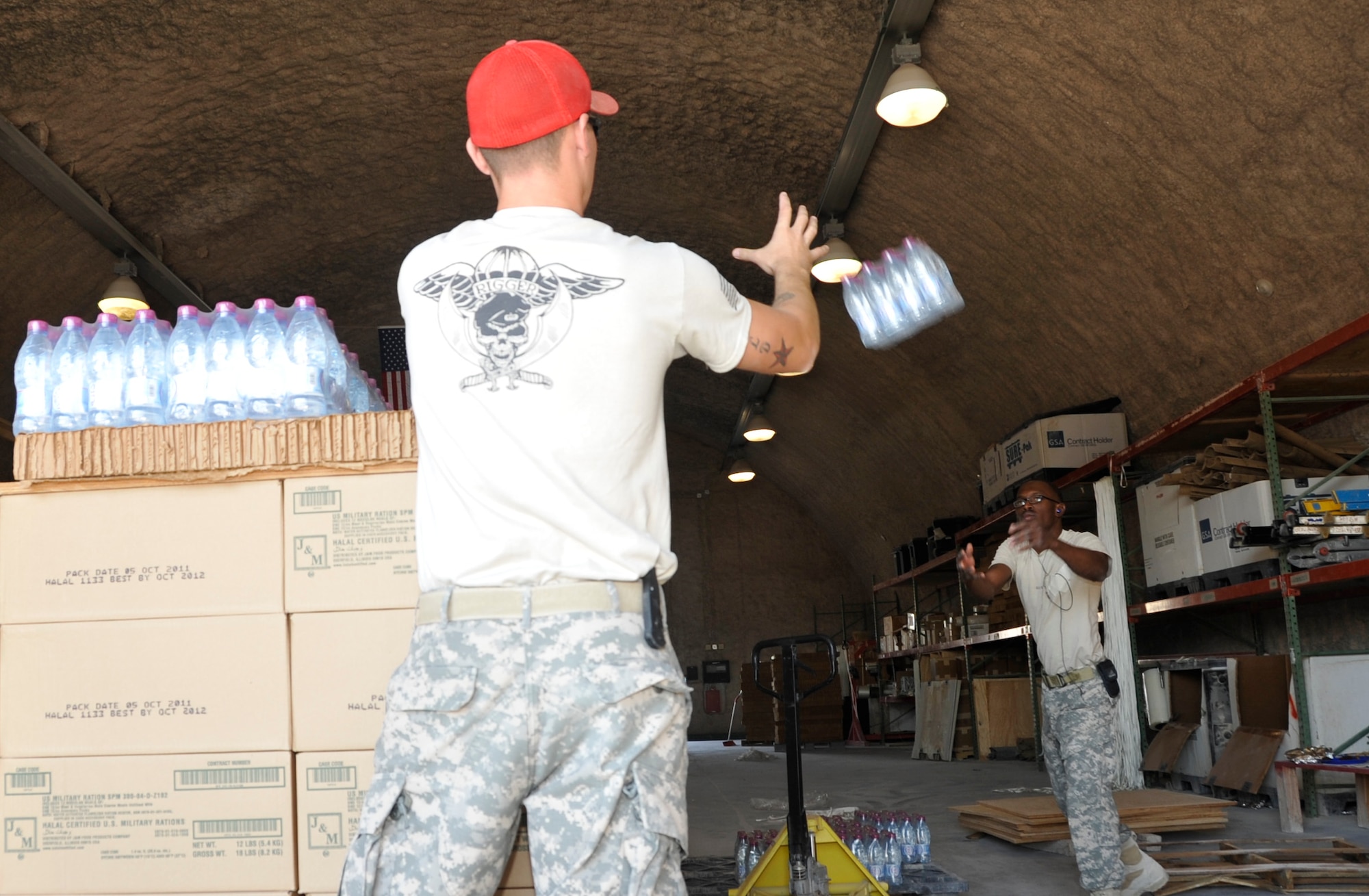 SOUTHWEST ASIA - Army Spc. Neilon Burton, 421st Quartermaster Company Detachment 4 Airdrop specialist, tosses Sgt. Jack Arnold, 421st QM Det. 4 shop foreman, a case of bottled water to stack on top of a bundle Dec. 4. The team essentially plays a game of Tetris with items being bundled to ensure they meet specific weight and size requirements before they can be loaded onto an aircraft and dropped to ground troops in Afghanistan. The detachment has airdropped more than 7,400 bundles, weighing more than 12 million pounds since the beginning of 2012. Burton, a native of the U.S. Virgin Islands, and Arnold, a native of Warner Robins, Ga., are both deployed from Fort Valley, Ga. (U.S. Air Force photo/Senior Airman Bryan Swink)