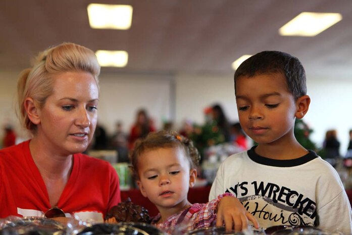 Maddy Halton, a volunteer with the non-profit organization Children Giving Gifts, escorts Ashley and John Willis, during a gift-giving event at the 5th Marine Regiment Instructional Facility, December 1, 2012. The event gave younger children a chance to select and wrap a free gift for their parents. Ashley and John were picking out gifts for their father, Staff Sgt. Edon Willis, who is currently deployed with 31st Marine Expeditionary Unit.