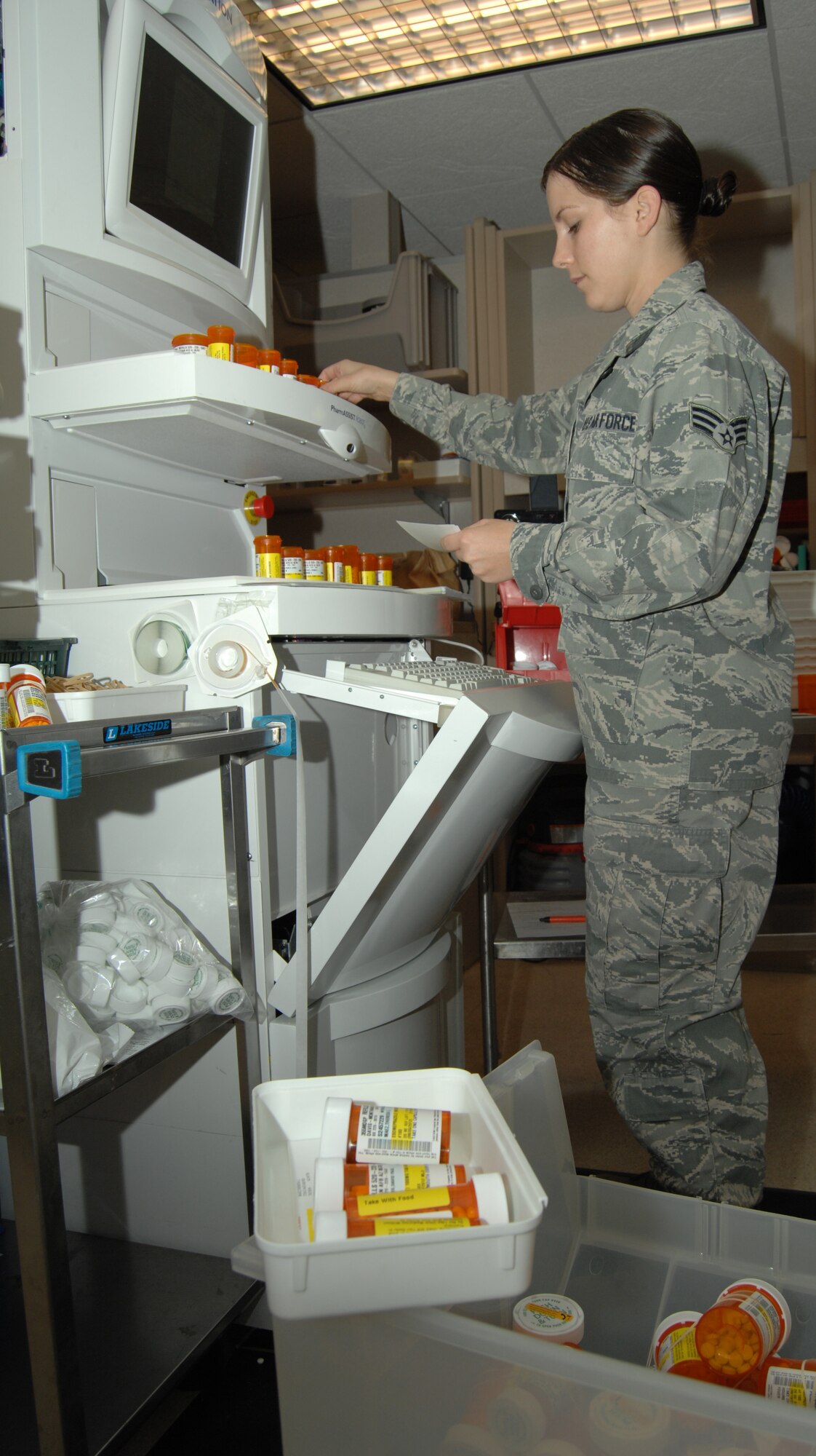 U.S. Air Force Senior Airman Samantha Womble, 355th Medical Support Squadron pharmacy technician, uses a machine to fill prescriptions on Davis-Monthan Air Force Base, Ariz., Nov. 27. The machine uses a robotic arm to accurately fill prescription bottles. (U.S. Air Force photo by Senior Airman Michael Washburn/Released)