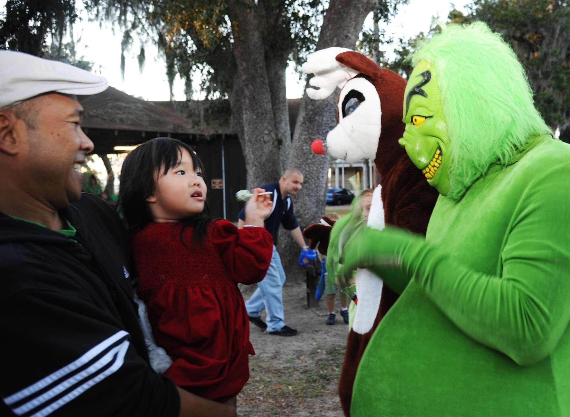 Navy Chief Petty Officer Same Saesing, Sup Ship Gulf Coast, Pascagoula, Miss., holds his daughter, Lilylani,3, as she is given a lollipop by the Grinch during Keesler’s annual Holiday in the Park, Dec. 6, 2012, at marina park, Keesler Air Force Base, Miss. The event included a tree lighting ceremony, hay rides, holiday music, visits with Santa and free food and beverages.  (U.S. Air Force photo by Kemberly Groue)