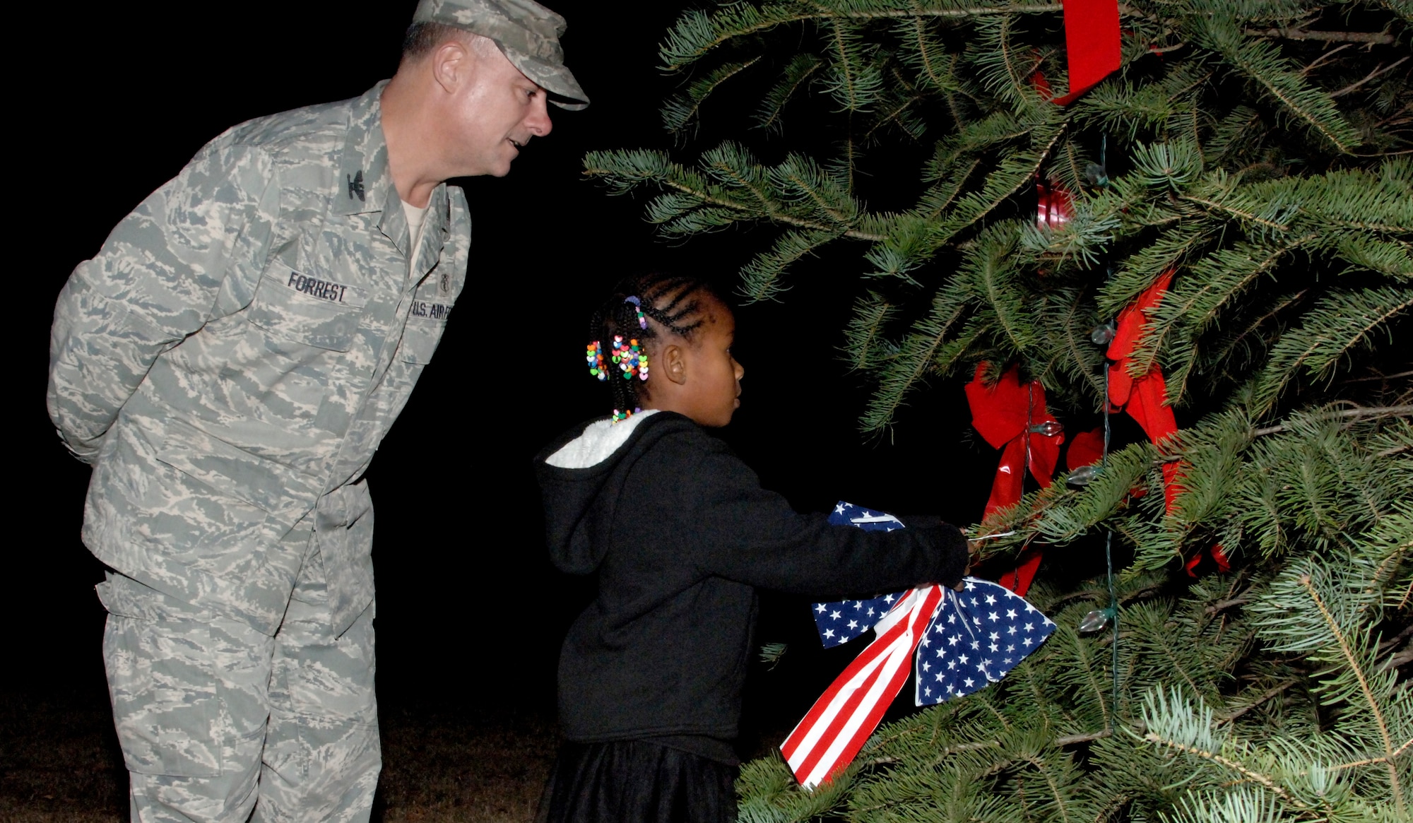 Col. Jim Forrest, Air Combat Command 633rd Medical Group deputy group commander, assists Jasmine E. Goodrum, daughter of Tech. Sgt. Aaron N. Goodrum, 633rd Air Base Wing noncommissioned officer in charge of chapel operations, in tying on a ribbon to the Christmas tree during the lighting ceremony at Langley Air Force Base, Va., Dec. 4, 2012. This was the 45th year running for this Christmas Tree Lighting Ceremony at Langley. (U.S. Air Force photo by Airman 1st Class Victoria Taylor/Released) 