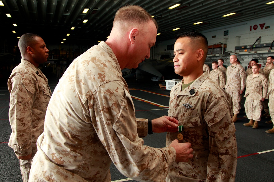 Colonel Scott D. Campbell, commanding officer, 15th Marine Expeditionary Unit, pins a Navy and Marine Corps Commendation Medal on Hospital Corpsman 2nd Class Wendell Tabios, during the Command Element’s promotion and awards ceremony in the hangar bay of the USS Peleliu, Dec. 1. Tabios received the award for his immediate medical response after a head-on collision on Camp Pendleton in July, where he saved a life.  The 15th MEU is deployed as part of the Peleliu Amphibious Ready Group as a U.S. Central Command theater reserve force, providing support for maritime security operations and theater security cooperation efforts in the U.S. 5th Fleet area of responsibility. Tabios, 37, is from Cavite, Philippines. (U.S. Marine Corps photo by Cpl. John Robbart III/Released) 