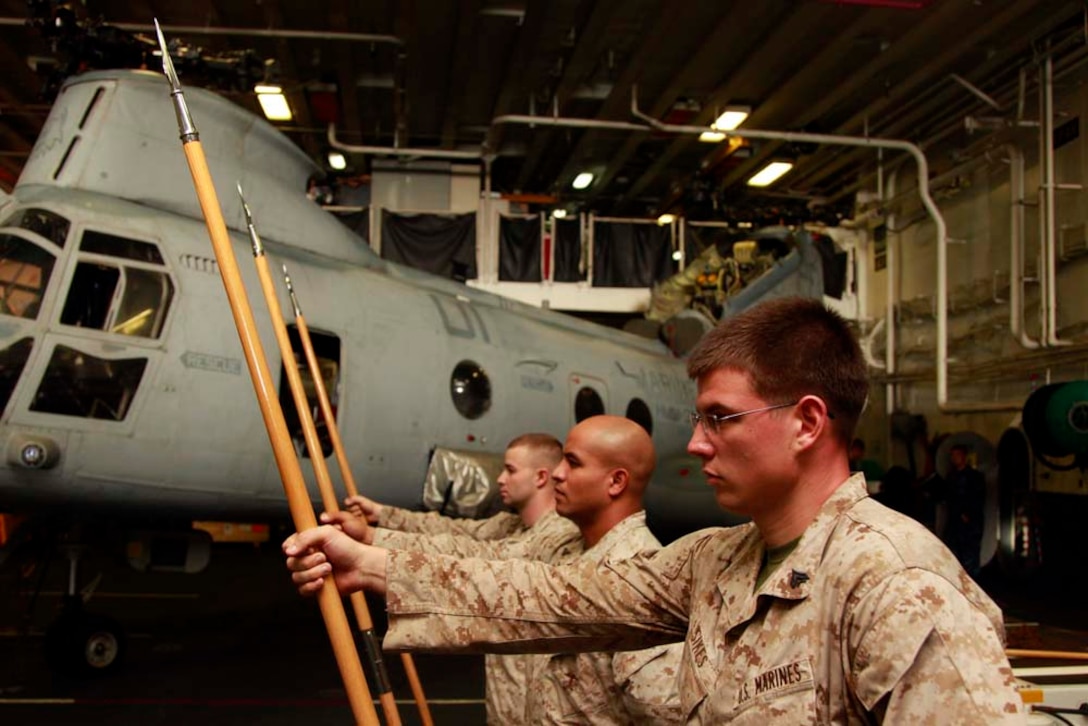 (Right to left) Cpls. Derek M. Sikes, Jeremy T. Ene, and Nicholas B. Watson, all with the 15th Marine Expeditionary Unit's Corporal's Course, practice guidon manual in the hangar bay of the USS Peleliu during Corporal's Course, Dec. 3. Corporals' Course is a professional military education for enlisted Marines designed to give them the tools to become better effective small unit leaders. The 15th MEU is deployed as part of the Peleliu Amphibious Ready Group as a U.S. Central Command theater reserve force, providing support for maritime security operations and theater security cooperation efforts in the U.S. 5th Fleet area of responsibility. Sikes, 22, is from Nashville, Tenn., Ene, 25, is from Oxnard, Calif., and Watson, 25, is from Midfield, Mich. (U.S. Marine Corps photo by Cpl. John Robbart III)