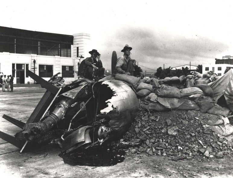 Army Air Forces Private First Class Raymond Perry (left, with binoculars) and AAF Cpl. Howard Marquardt, of South Dakota, man another gun emplacement, hastily constructed in front of Hangar 5 shortly after the Japanese raid on Oahu. A burned-out aircraft engine, sand bags, table, and debris from the attack made up the construction material for this bunker. (Courtesy photo)