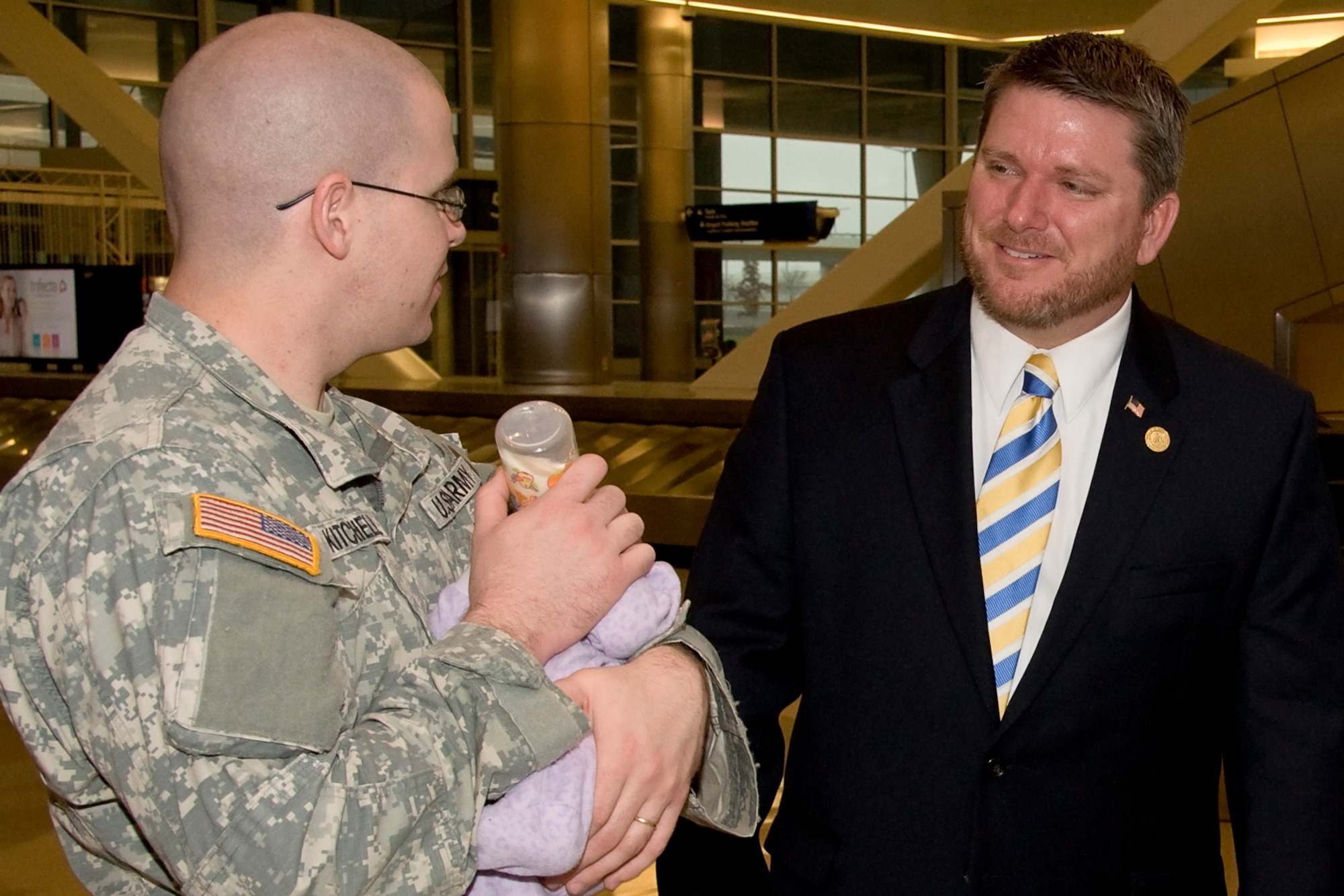 GRISSOM AIR RESERVE BASE, Ind. -- Spc. John Kitchell, 316th Psychological Operations Company psychological operations specialist, feeds his two-week old daughter, Claire, while speaking with Indiana State Rep. Kevin Mahan after a deployment ceremony at Indianapolis International Airport Dec. 7. Twenty Four Soldiers, including Kitchell left Indianapolis to conduct additional training at Fort Dix, N.J., to prepare for a 10-month deployment in the Horn of Africa in support of Operation Enduring Freedom. (U.S. Air Force photo/Staff Sgt. Ben Mota)
