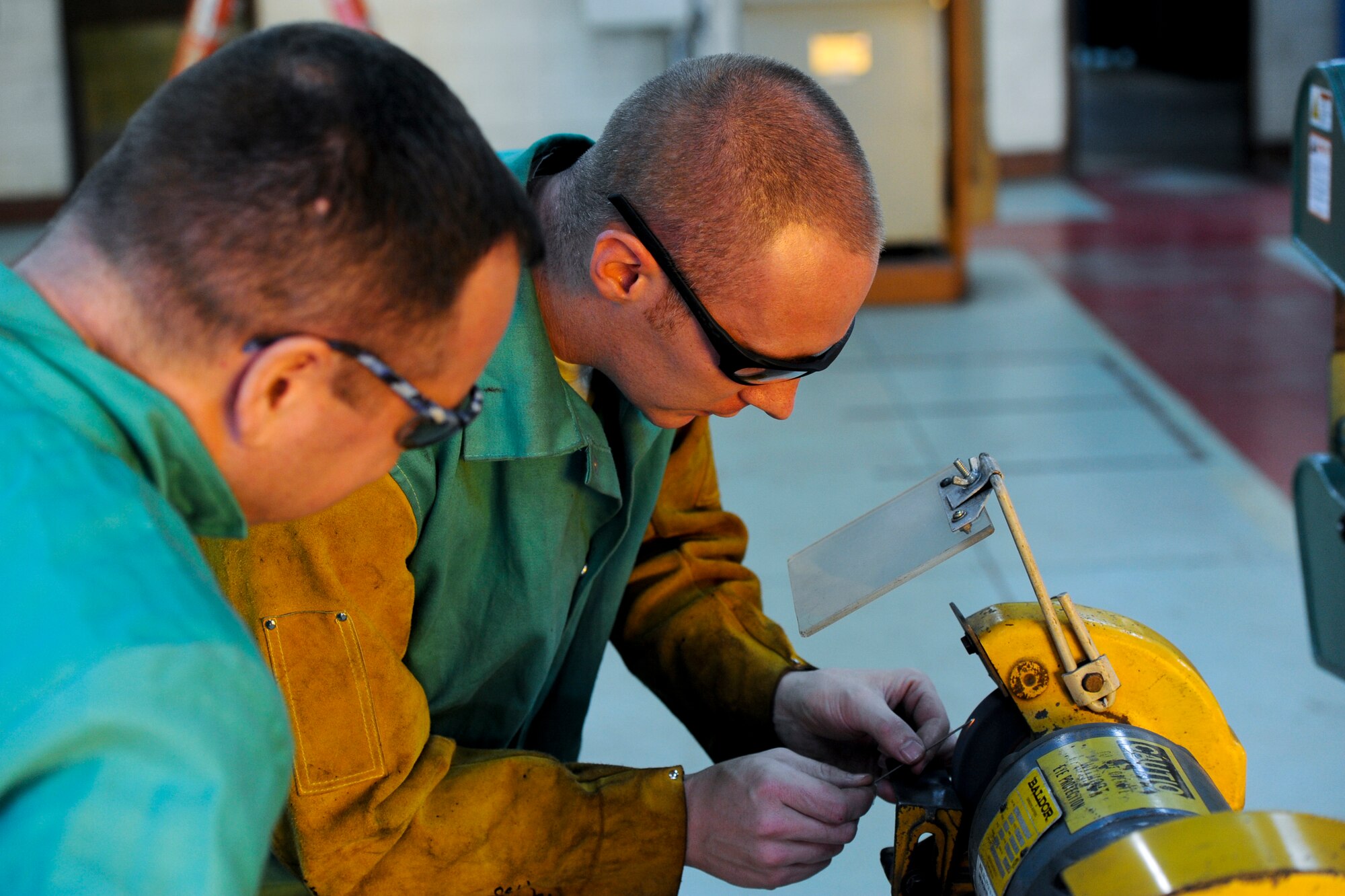 U.S. Air Force Staff Sgt. Justin Costanzo, 18th Equipment Maintenance Squadron aircraft metals technology craftsman, shows Col. Brian McDaniel, 18th Wing vice commander, how to use the pedestal grinder on Kadena Air Base, Japan, Dec. 6, 2012. The pedestal grinder is a grinder mounted on a pedestal that is bolted to the floor. Pedestal grinders are commonly used to hand grind cutting tools and to perform other rough grinding tasks. (U.S. Air Force photo/Airman 1st Class Justin Veazie)