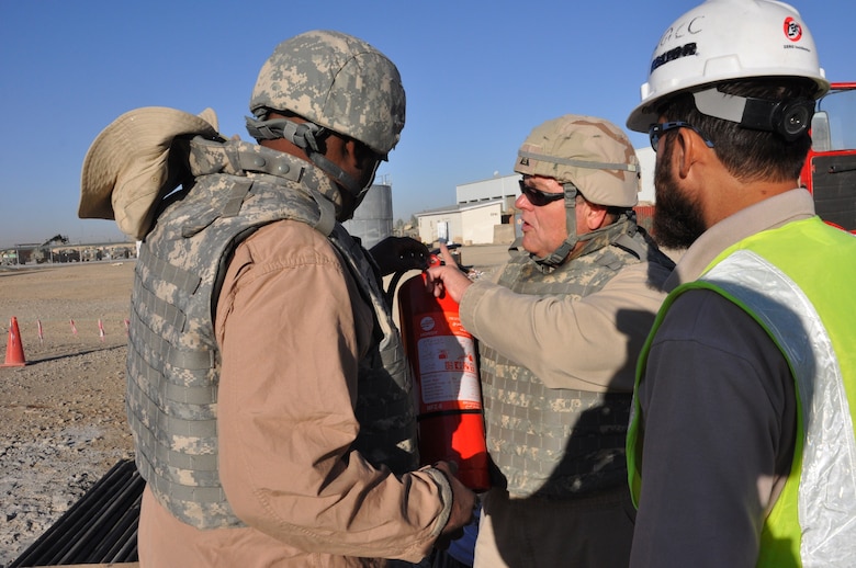 Jeff Ice, a safety and occupational health specialist who deployed to Kandahar from the USACE New York District shows an Afghan construction worker how to detect a fake fire extinguisher. Some counterfeit ones, instead of releasing the normal fire-stopping agent they are supposed to release, spit out flour or other non-effective substances.