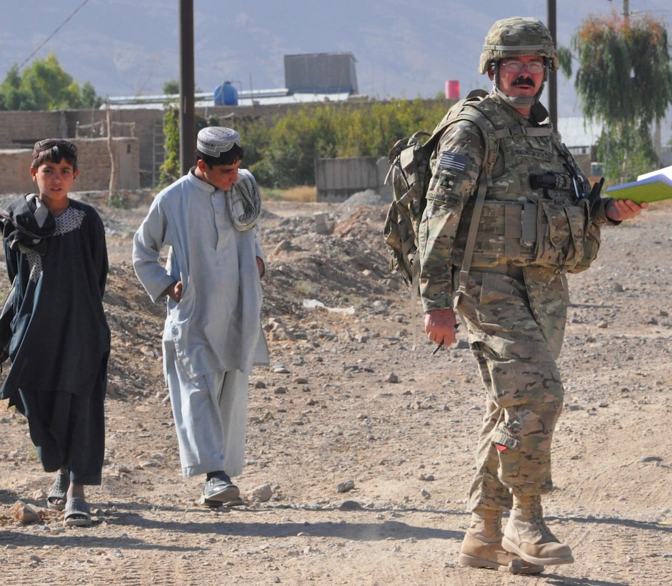 A civil engineer from the 565th Engineer Detachment Forward Engineer Support Team - Advance visually inspects the unpaved road at Shur Andam Industrial Park, as two boys from a local village follow him. The goal is for the Government of the Islamic Republic of Afghanistan and/ or a donor nation to use the data Hollingsworth provides to build a paved road at the industrial park.