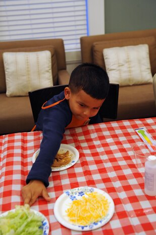 Angel, 6, reaches for tomatoes to make his burrito face during the Kids in the Kitchen on Monday at the McHugh Woods Community Center. The Exceptional Family Member Program and Families Over Coming Under Stress joined to show the children how to talk about their feelings with burrito making.
