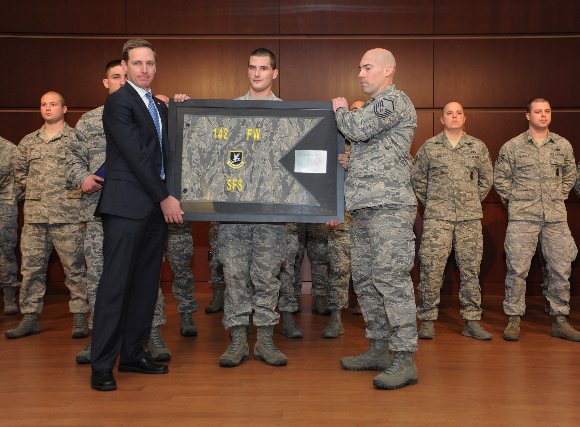 Mr. Cameron Smith receives a framed unit guidon from Oregon Air National Guard Master Sgt. Derek Moore, 142nd Fighter Wing Security Forces Squadron, during the mobilization ceremony for the 142nd Fighter Wing Security Forces Squadron at Camp Withycombe, Ore., Dec. 11, 2012. Smith represented Oregon Governor John Kitzhaber for the ceremony and the unit guidon is on behalf of the entire group deploying as a reminder that Oregon’s sons and daughters are proudly answering the nation’s call. (U.S. Air Force photograph by Tech. Sgt. John Hughel, 142nd Fighter Wing Public Affairs/Released)
