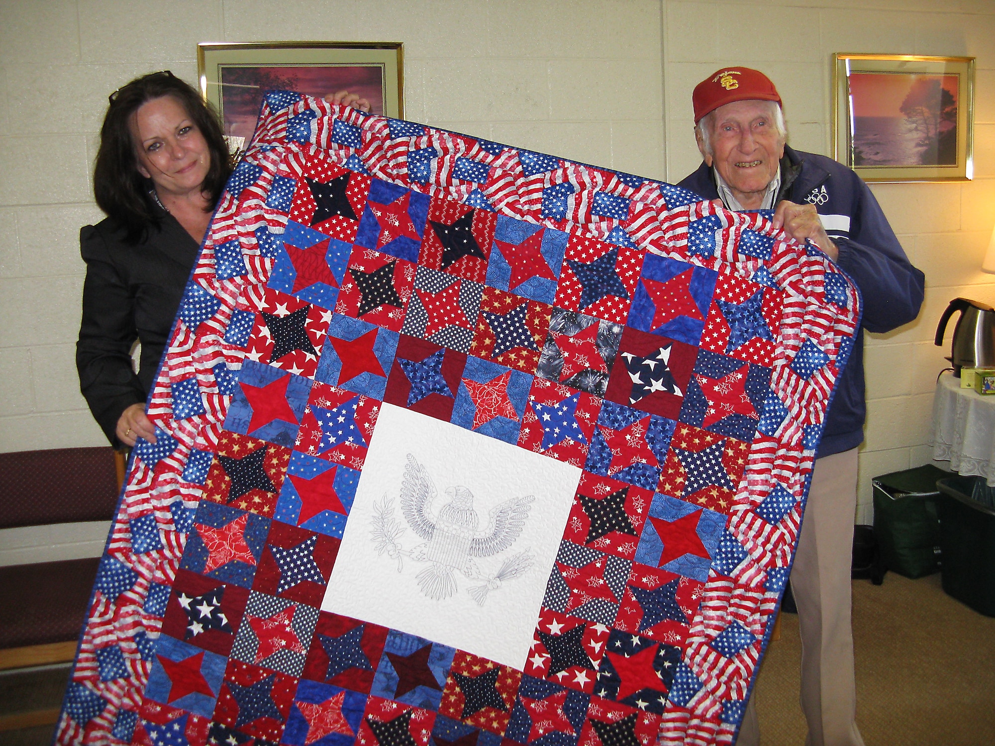 Janice Laurenti, Air Force Test Center Contracting Directorate contracts specialist and Quilts of Valor Foundation Southern California regional coordinator, presents Louis Zamperini with a quilt following his appearance at the Base Theater. (Courtesy photo by Col. Christopher Azzano)