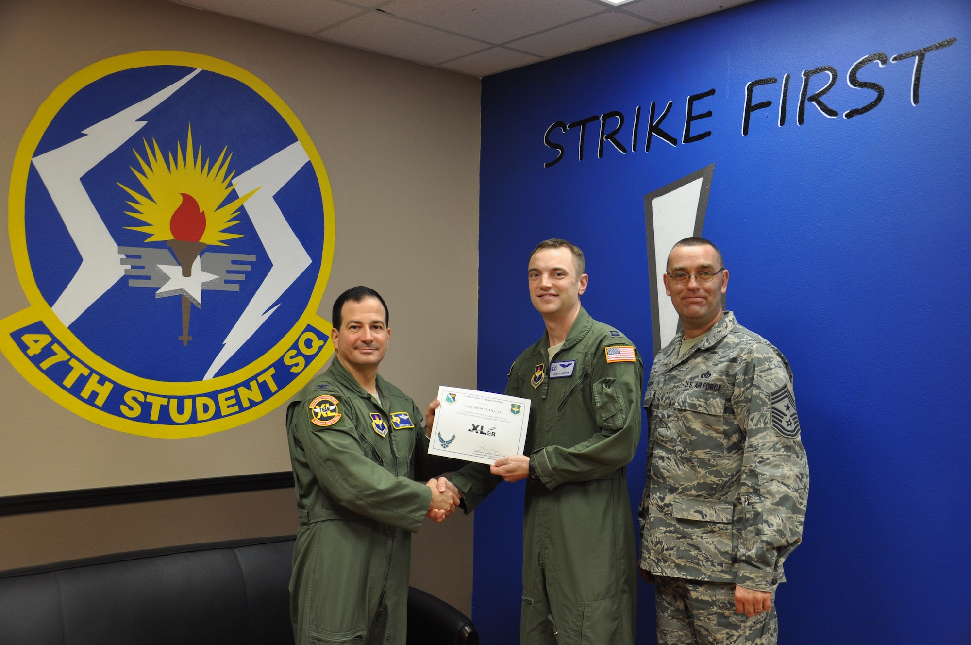 Accepting the award on behalf of himself and Capt. Wiley is Capt. Justin Hrynyk, 47th Student Training Squadron grad flight commander and graduation officer, he poses with Col. Mark Doria, 47th Flying Training Wing vice commander, and Chief Master Sgt. Garry Berry, 47th FTW command chief, after being presented the XLer of the week award at Laughlin Air Force Base, Texas, Nov. 28, 2012. The XLer is a weekly award chosen by wing leadership and given to those who consistently make outstanding contributions to Laughlin and their unit. (U.S. Air Force photo/2d Lt. David Tart)