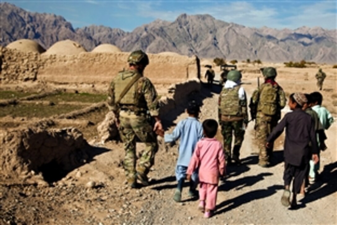 Afghan children walk alongside a coalition force member during a presence patrol in Farah province, Afghanistan, Dec. 9, 2012.