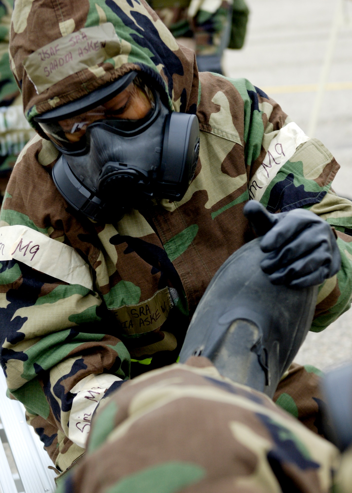 U.S. Air Force Senior Airman Sandra Askew, 633rd Surgical Squadron women’s health clinic, removes an Airman’s boot during a simulated chemical attack at Langley Air Force Base, Va., Dec. 12, 2012. During this phase I command unit exercise, players were instructed to break into pairs and assist each other through the simulated-chemical decontamination process stations. (U.S. Air Force photo by Airman Kimberly Nagle/Released)