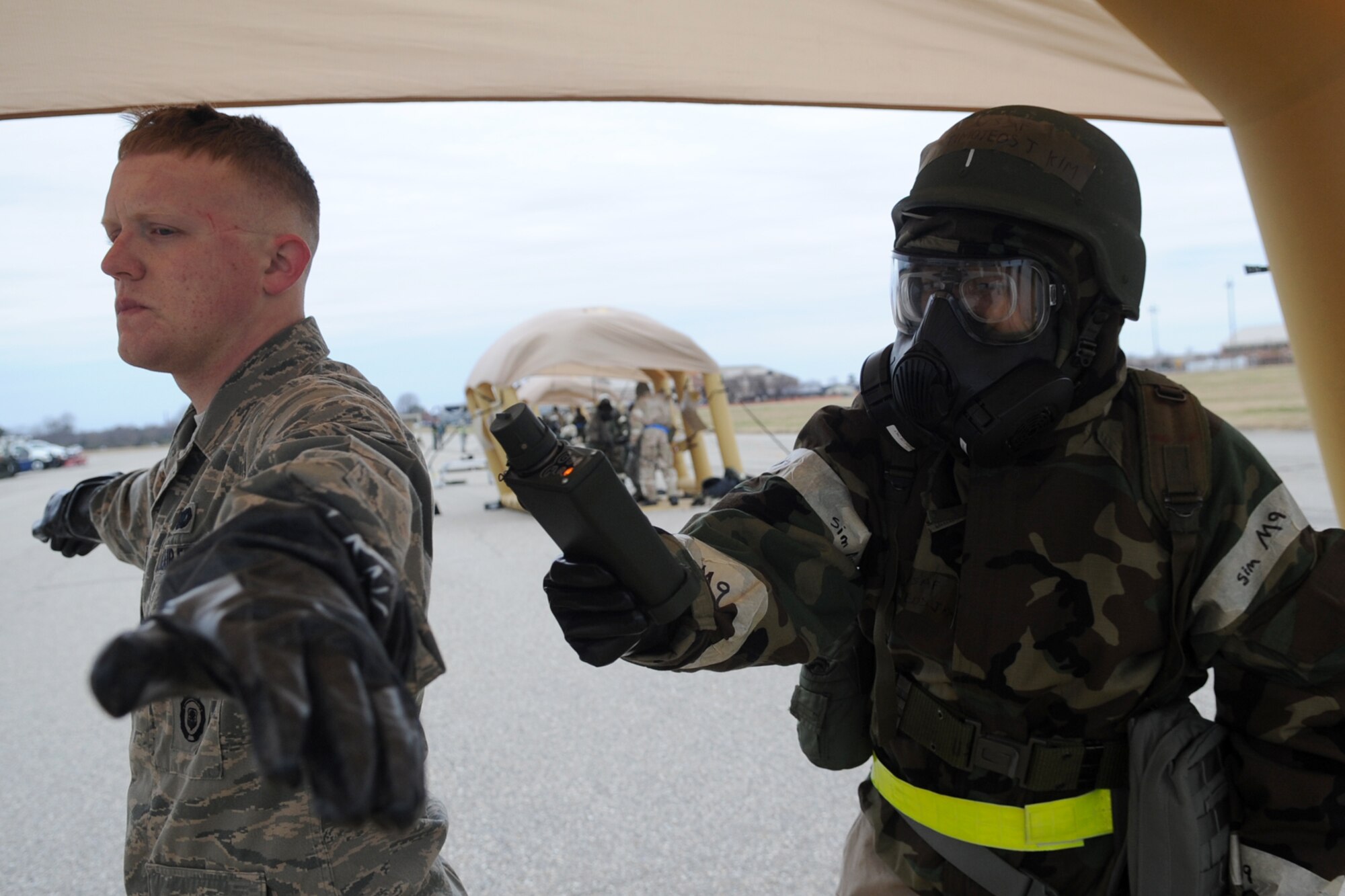 U.S. Air Force Airman 1st Class Timoteos Kim, (right) 633rd Logistics Readiness Squadron fuel distribution flight member, monitors Airman 1st Class Jerry Tondini, (left) 633rd Security Forces Squadron installation entry controller, with a Point Source Chemical Detector during a combined unit exercise at Langley Air Force Base, Va., Dec. 12, 2012. The chemical decontamination process included four zones—red, orange, yellow and blue—to ensure proper removal of simulated-contaminated mission orientated protective posture gear. (U.S. Air Force photo by Senior Airman Racheal E. Watson/Released)