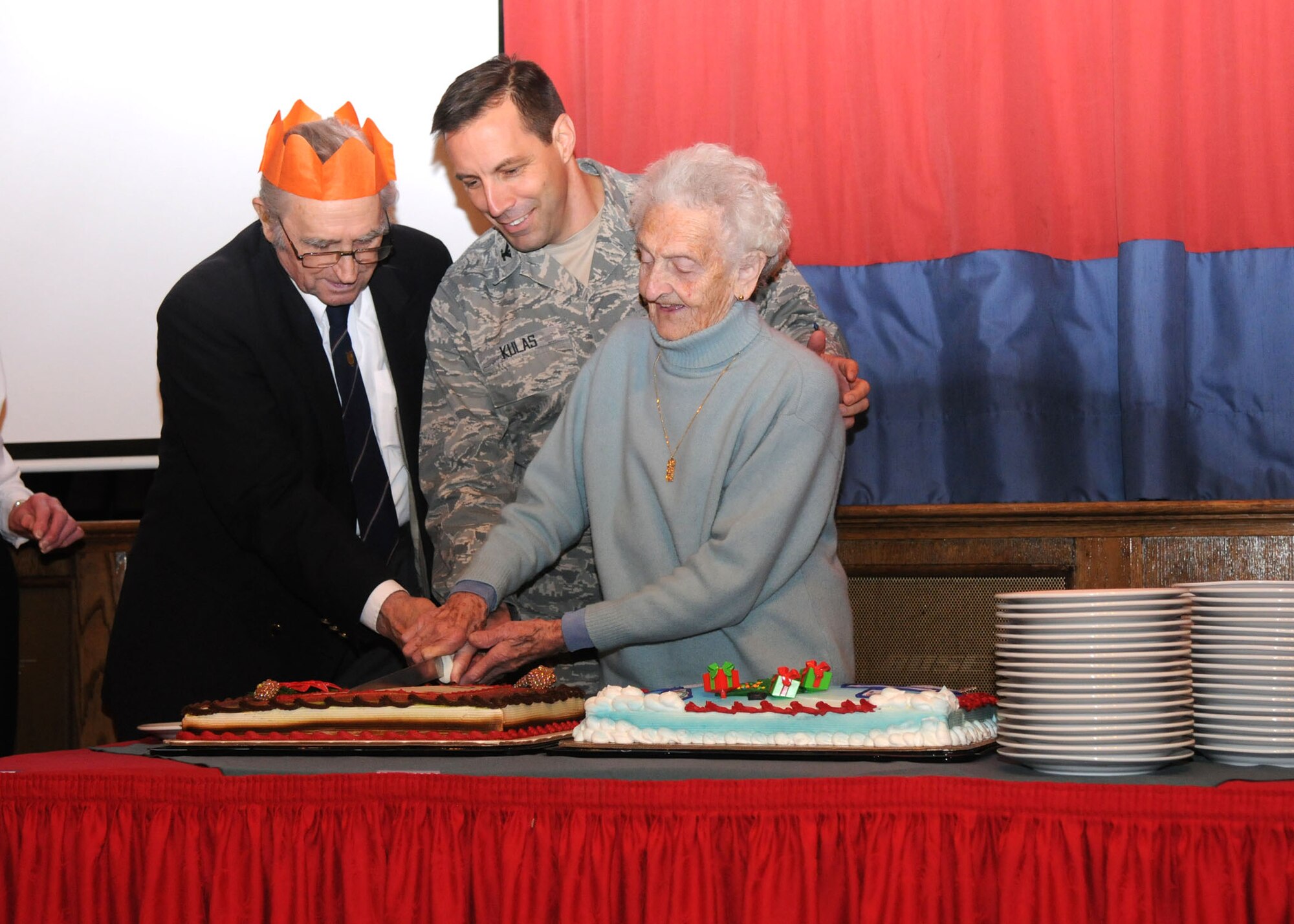 Col. Christopher Kulas, 100th Air Refueling Wing commander, cuts the cake at the Senior Citizens Christmas party with the help of Caroline Francks and Eugne Hiluk both from Mildenhall, Dec. 12, 2012, at RAF Mildenhall, England. This year marked the 31st anniversary of the Senior Citizens Christmas party on RAF Mildenhall. (U.S. Air Force photo by Airman 1st Class Kelsey Waters/Released)