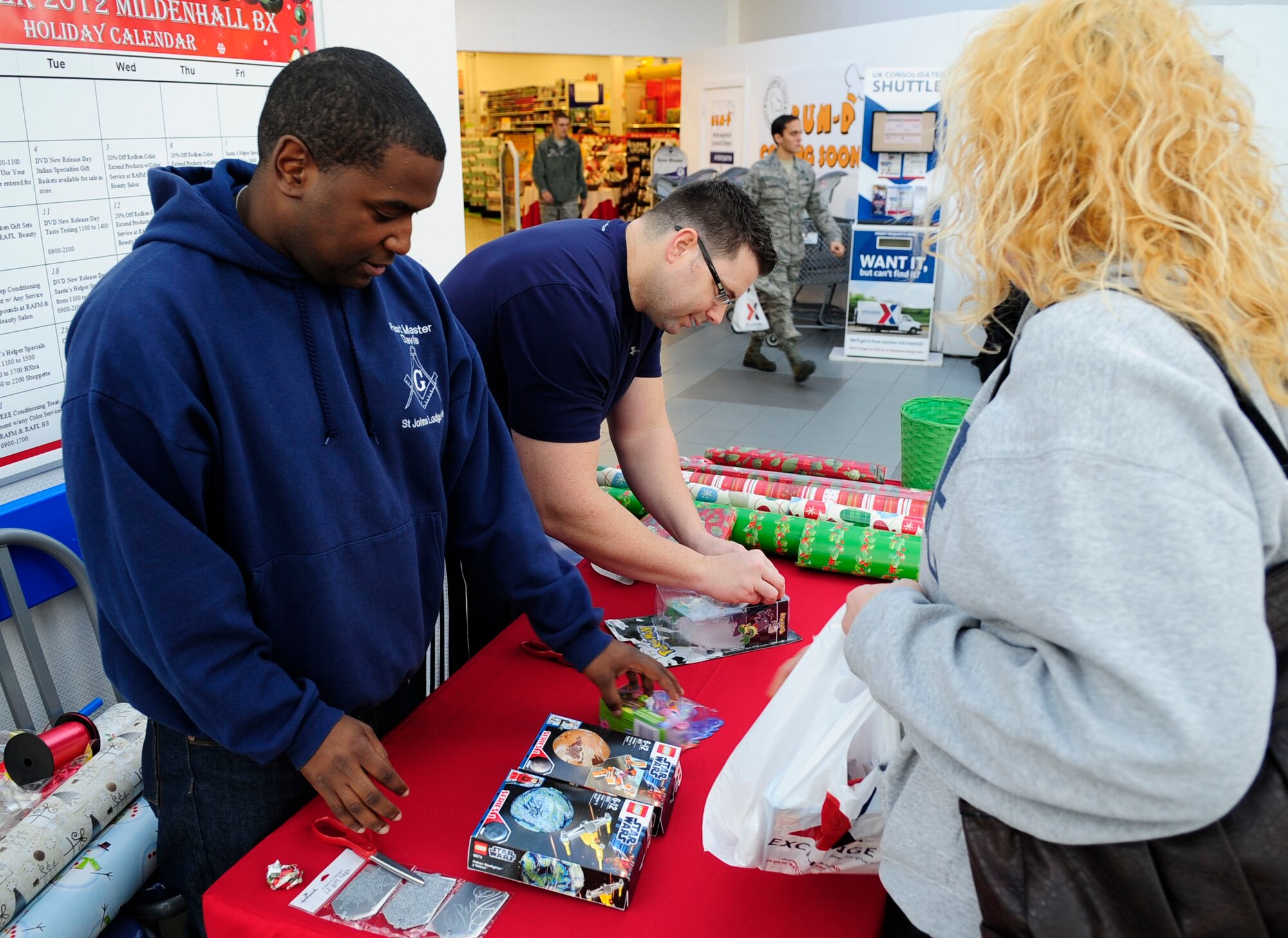 Staff Sgt. Michael Davis, 100th Maintenance operations Squadron NCO in charge of scheduling maintenance training, and Master Sgt. Greg Gifford, 100th MOS training superintendent, both from Chicago, wrap gifts for a customer Dec. 11, 2012, at the B-Xtra on RAF Mildenhall, England. Every year, volunteers from around Team Mildenhall offer gift wrapping assistance to customers at the B-Xtra during the holiday season. (U.S. Air Force photo by Airman 1st Class Dillon Johnston/Released)