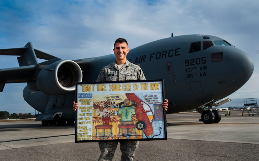 Senior Airman Joshua Douglass, 437th Aircraft Maintenance Squadron maintainer, holds his winning poster 'Don't take your car to the bar' that he drew, Dec. 6, 2012 on Joint Base Charleston - Air Base flightline. Douglass' poster is now posted in the five squadrons of the 437th AMXS, where Airman can see it every day . (U.S. Air Force photo/Airman 1st Class Ashlee Galloway)