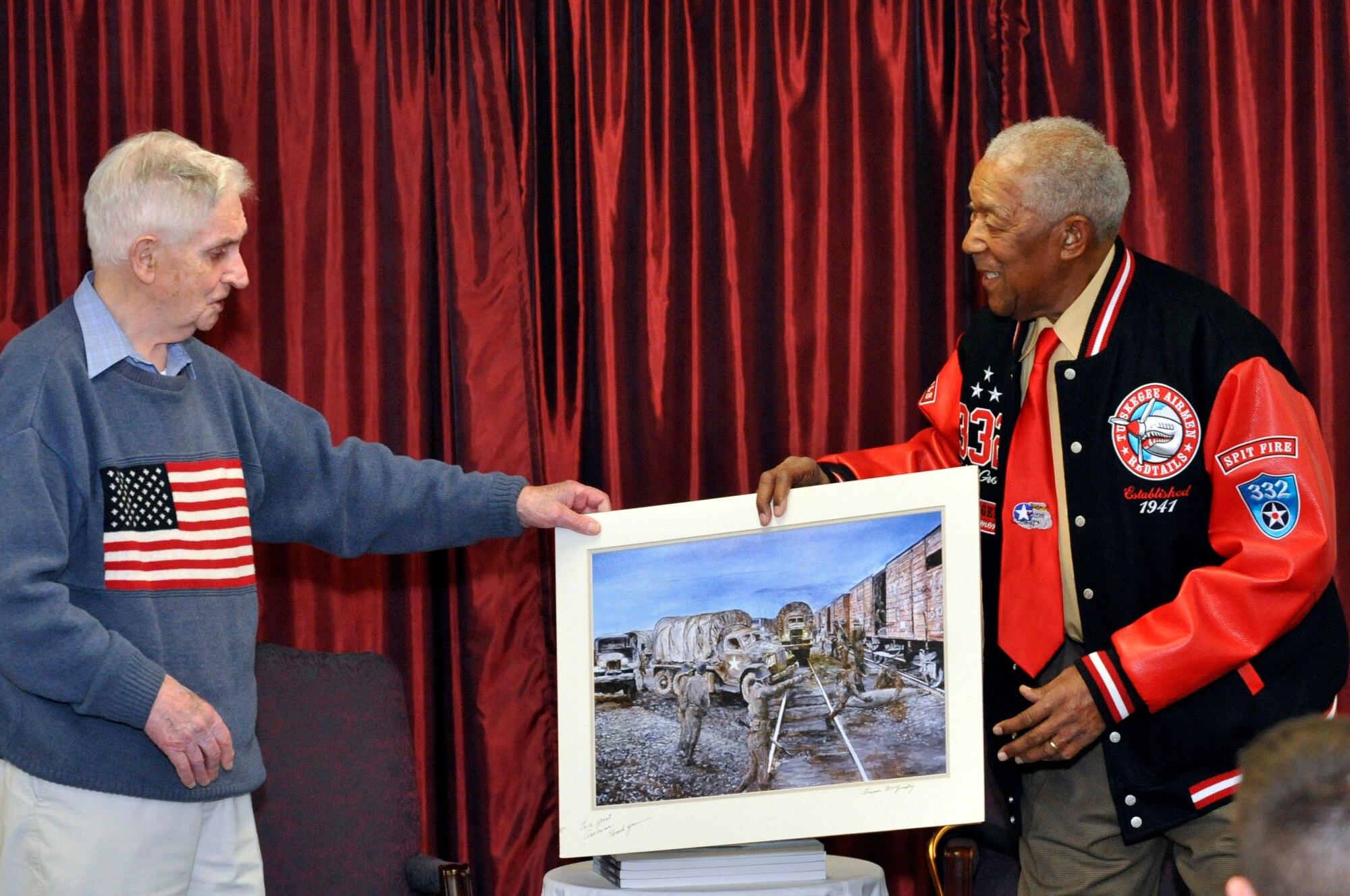 Francis "Frank" McGinley, New Jersey veteran and artist, presents retired Tech. Sgt. George Watson, documented original Tuskegee Airman, with a signed print of his painting depicting "The Great Train Robbery" Dec. 5, 2012, at the Kish Airman Leadership School on Joint Base McGuire-Dix-Lakehurst, N.J. The Air Force Sergeants Association Chapter 211's annual POW/MIA Remembrance included readings from McGinley's recently published book, “Let Us Never Forget: An Illustrated History of World War II.” McGinley used details from World War II veterans to illustrate their stories through his artwork, such as Watson and the Tuskegee Airmen's Great Train Robbery. (U.S. Air Force photo by Wayne Russell/Released)