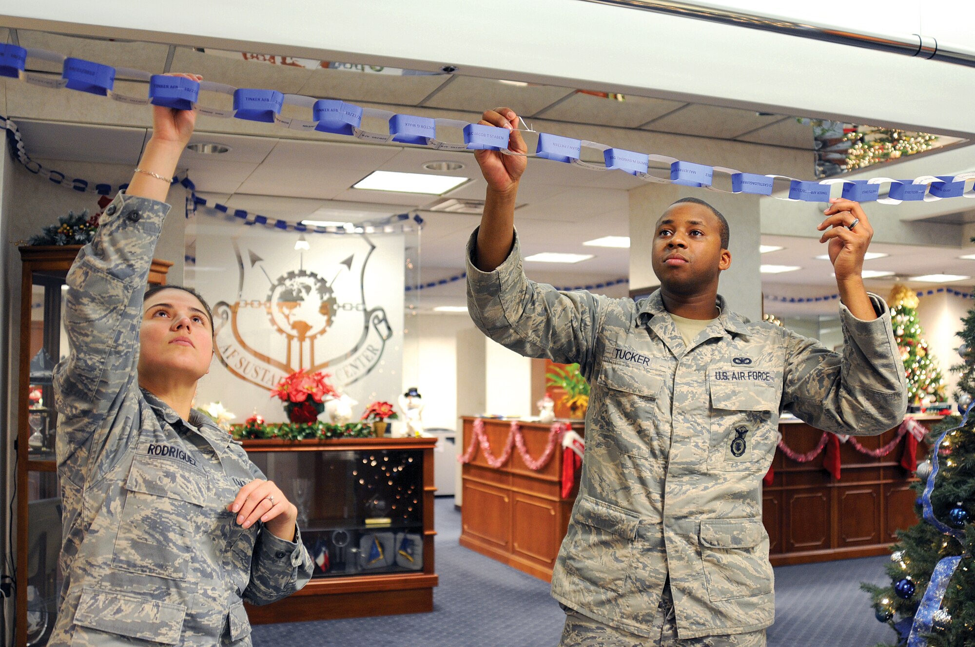 In the Air Force Sustainment Center command section, Bldg. 3001, Tech. Sgt. Maria Rodriguez and Staff Sgt. Ben Tucker hang a chain of paper links bearing names of 2,170 AFSC Airmen who deployed in 2012.  The links line the command section and continue out into the hallway, draped from the ceiling just inside the flagpole entrance. (Air Force photo by Margo Wright)