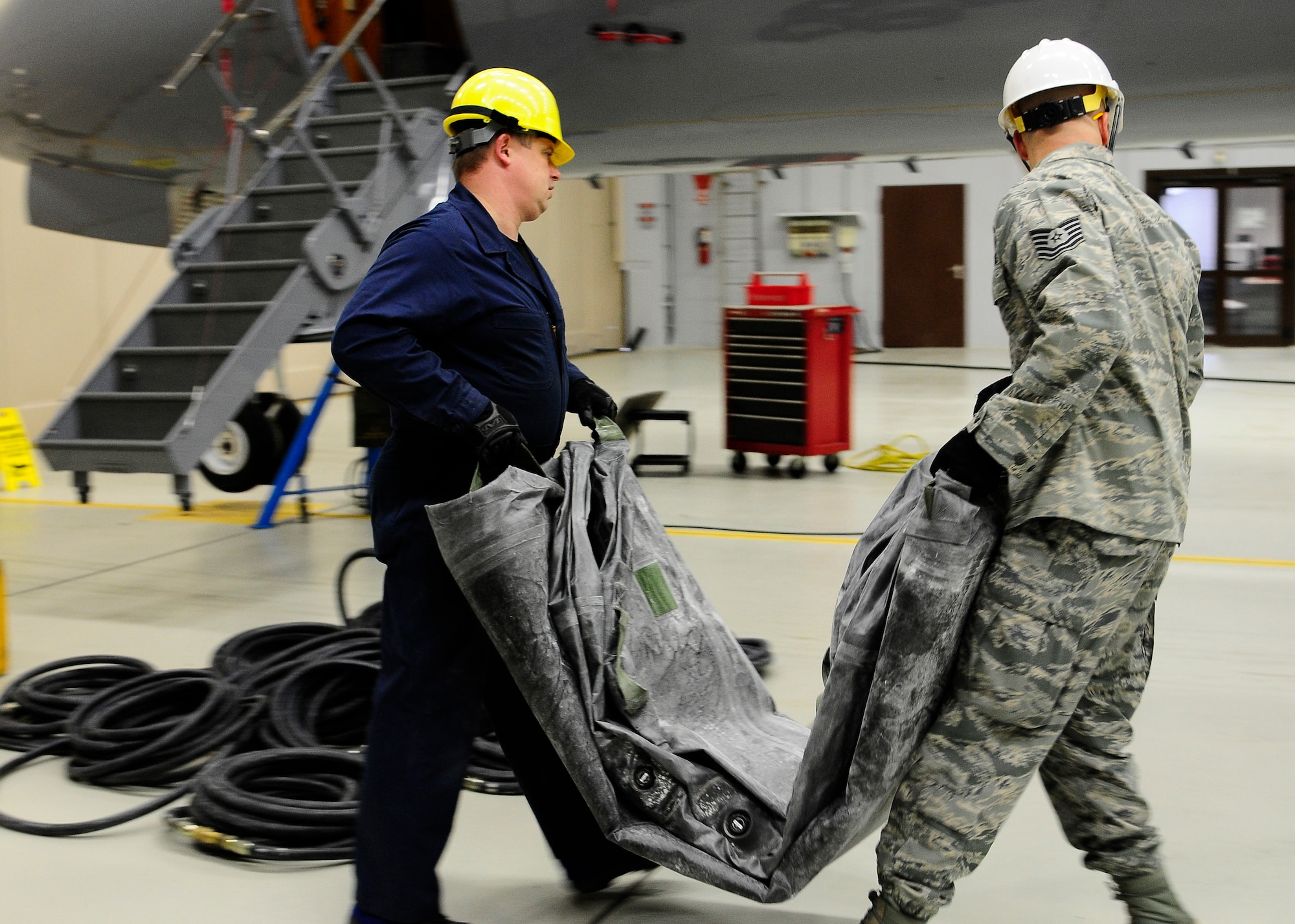 Tino Weichel (left), 86th Maintenance Squadron repair and reclamation craftsman, and Tech. Sgt. Jonathan Stone, 86th MXS repair and reclamation craftsman, carry the aircraft lifting bags into the position needed to lift the aircraft on Ramstein Air Base, Germany, Dec. 10, 2012. The black rubber aircraft lifting bags are used to lift aircraft in order to avoid potential damage. (U.S. Air Force photo/Airman 1st Class Hailey Haux)