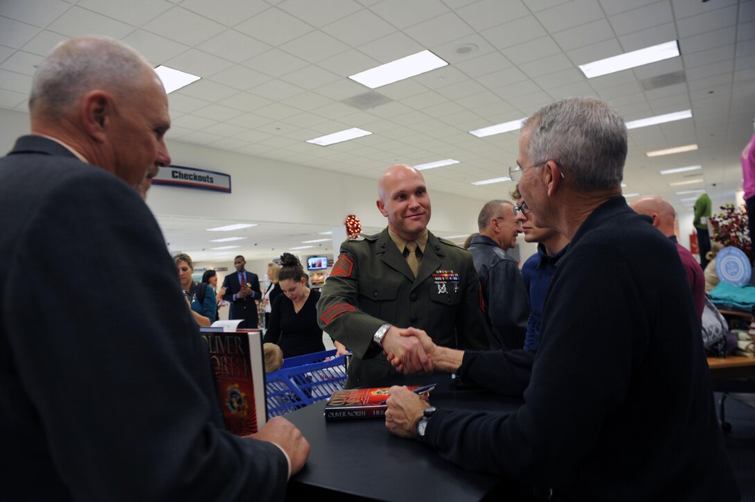 Retired Lt. Col. Oliver L. North, shakes hands with Staff Sgt. Clinton Fowler, S-4 chief, Security Battalion, during his new book “Heroes Proved” signing at the Marine Corps on Thursday. Fowler went with his father Steve Keene, retired master sergeant during the book signing.