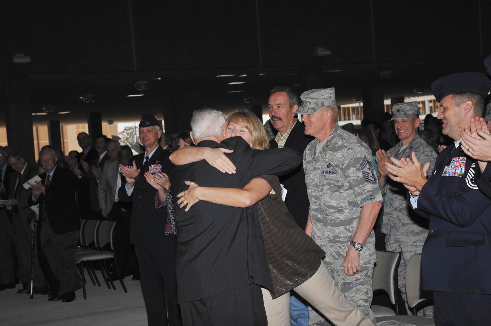 Chief Master Sgt. James Cody, AETC command chief, stands by as his wife, Athena, gets a hug from retired Chief Master Sgt. Robert Gaylor, keynote speaker for the event.  (US Air Force Photo by Mr. Alan Boedeker)