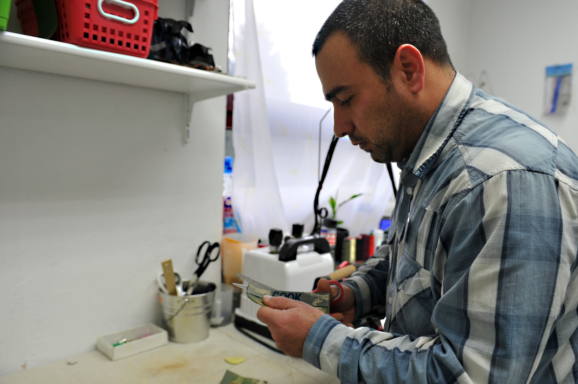 Dhiaa Zeidlr, owner of Bablon Alterations, cuts excess velcro backing from name tapes for Air Force uniforms at his shop on Ramstein Air Base, Germany, Dec. 14, 2012. The alterations shop serves the more than 54,000 members of the Kaiserslautern Military Community. (U.S. Air Force photo/Airman 1st Class Holly Cook)