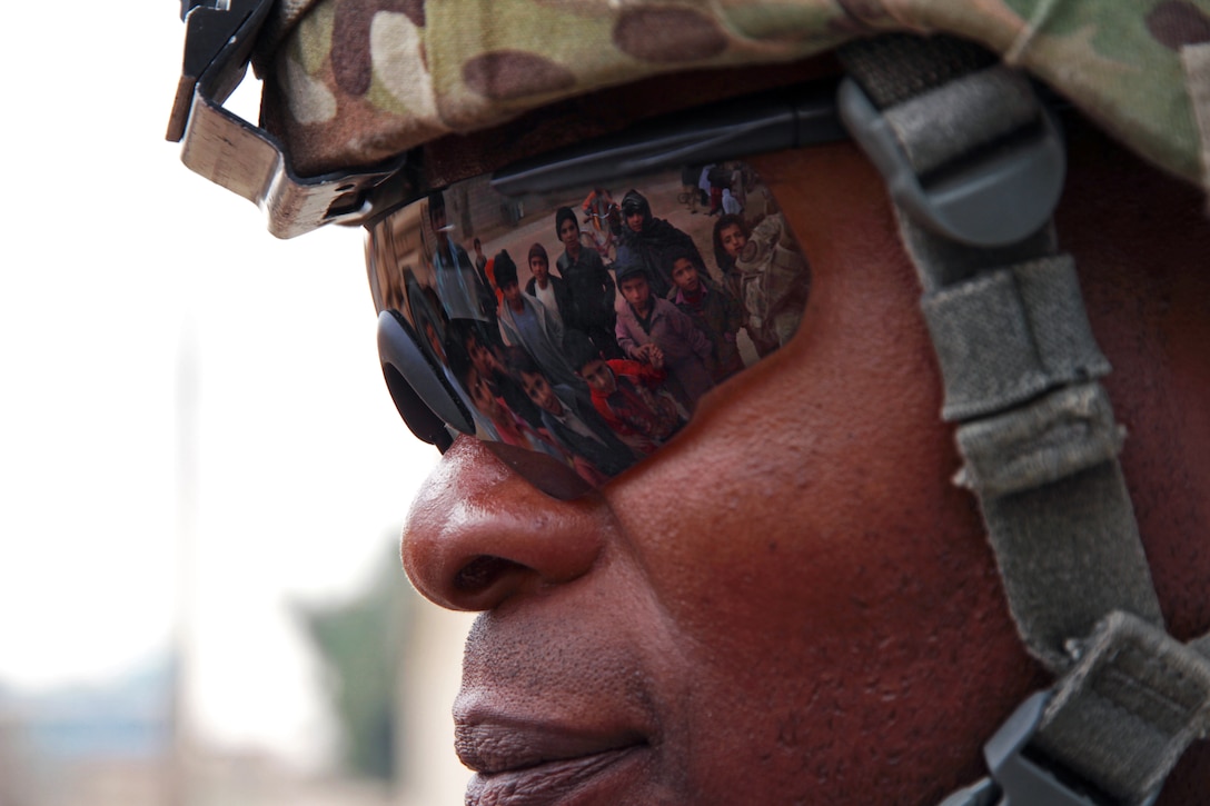 Afghan children are reflected in the sunglasses of U.S. Army Sgt. Roderick Cooper during a key leader meeting about counternarcotics in Farah, Afghanistan, Dec. 15, 2012. Cooper is assigned Provincial Reconstruction Team Farah.